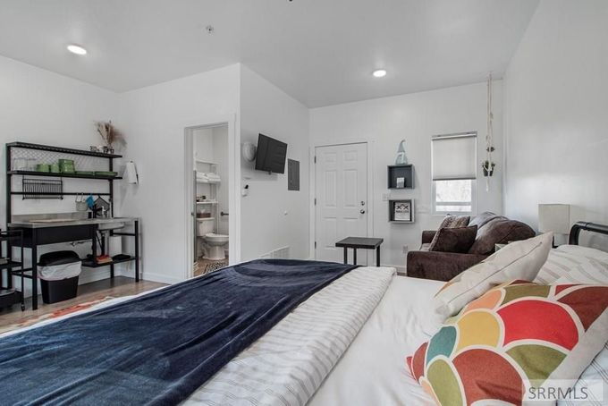 Bright bedroom with a white wicker chair, bed, large window, radiator, and open closet.