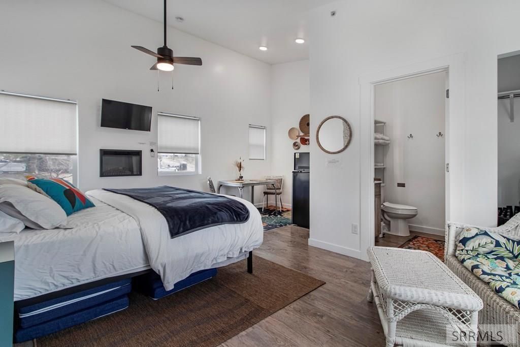 Cozy bedroom with a bed, wall-mounted TV, ceiling fan, and windows with blinds