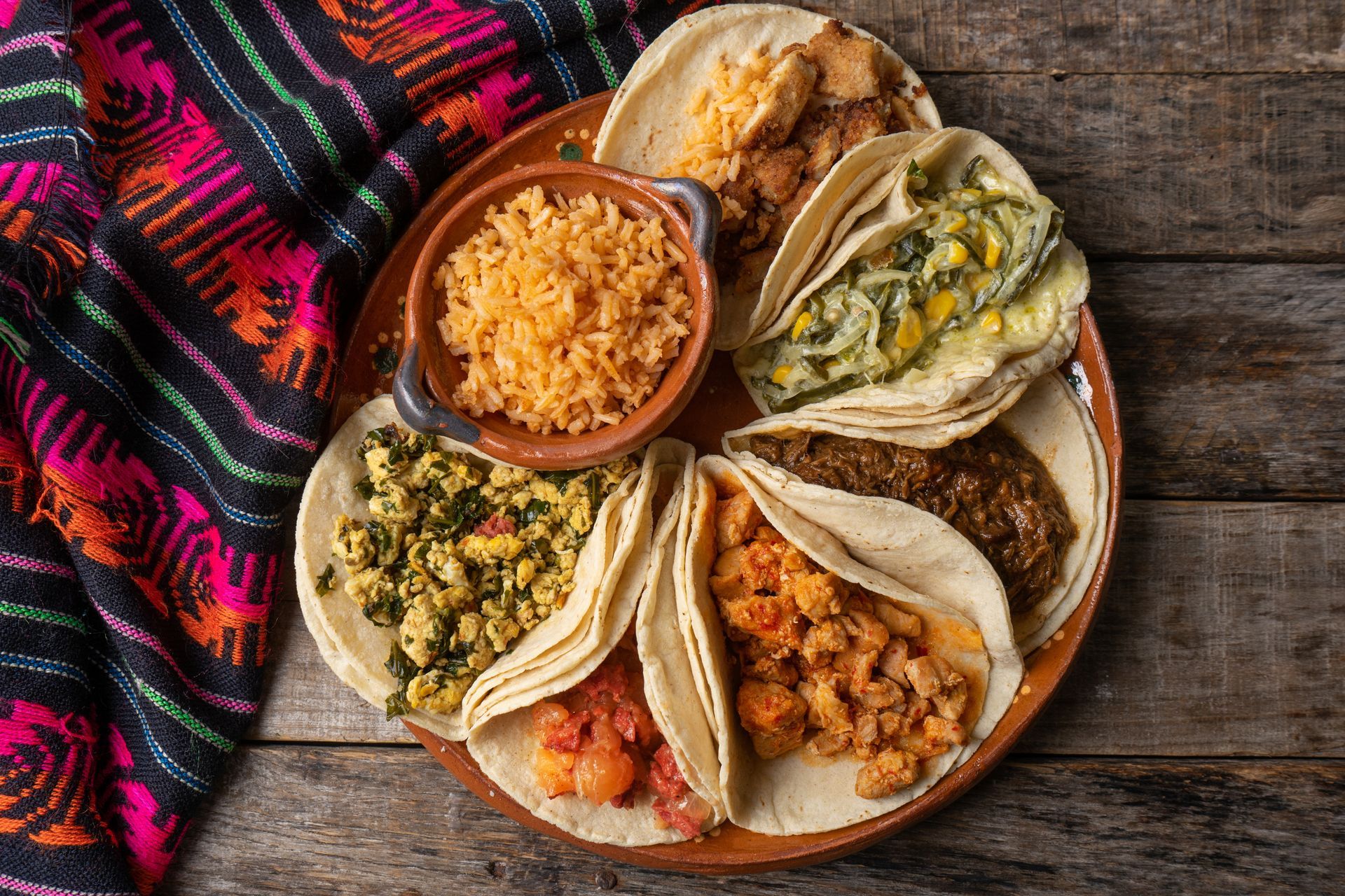 Mexican food platter with tacos, rice, and salsas on a rustic table