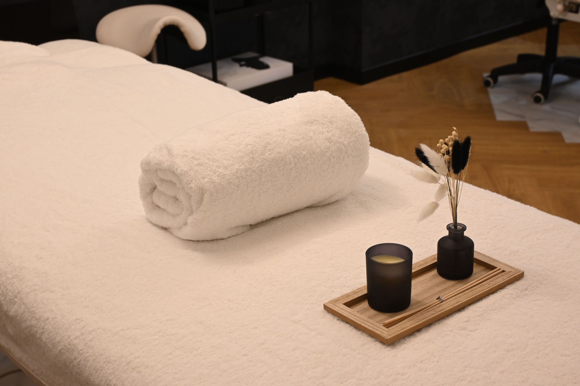 Neatly made bed with rolled white towel and black candle tray on the blanket