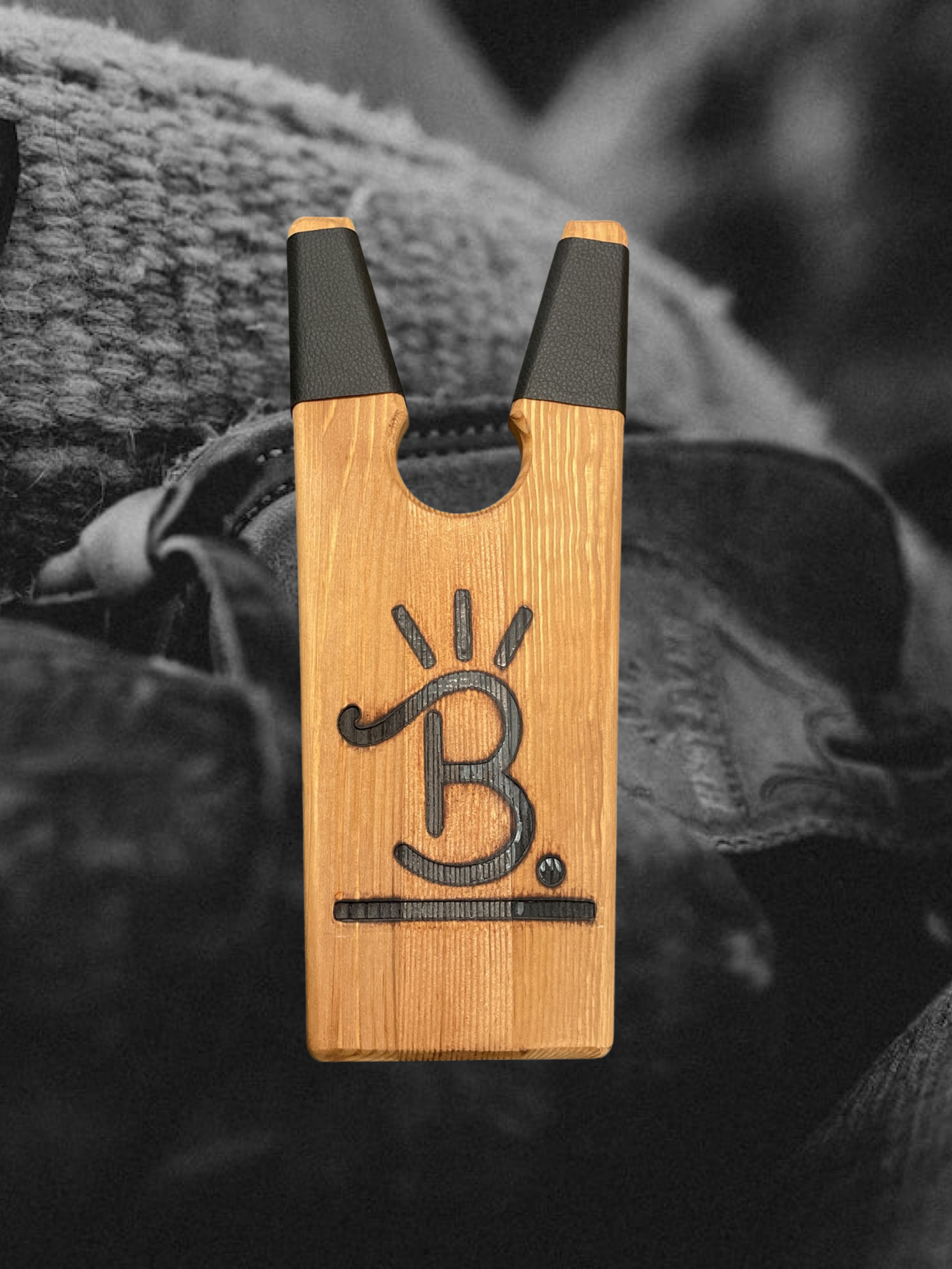 Wooden clip with a black symbol hangs from a dark strap against a gray knit background.