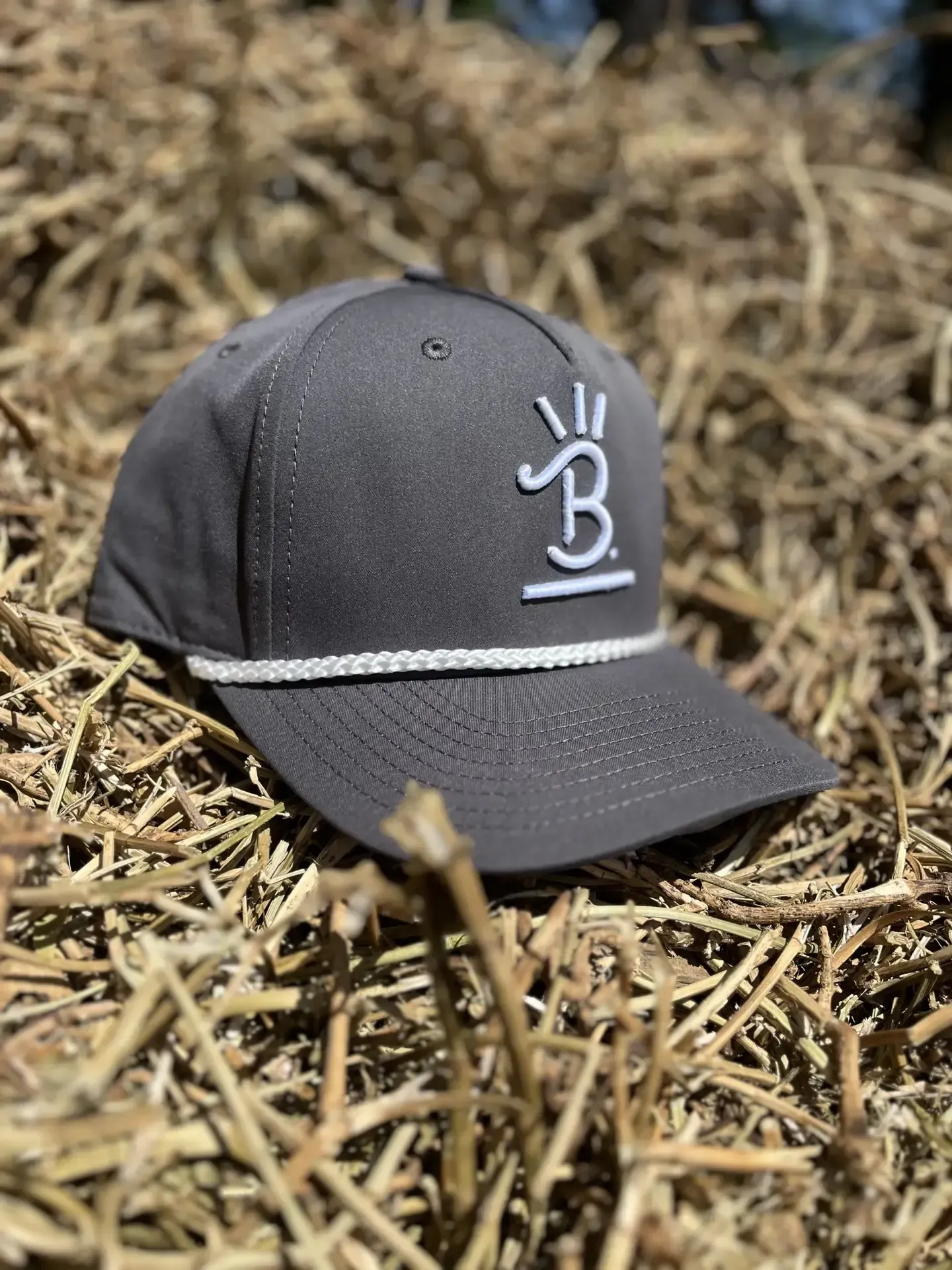 Gray cap with a white logo resting on straw or dry grass outdoors