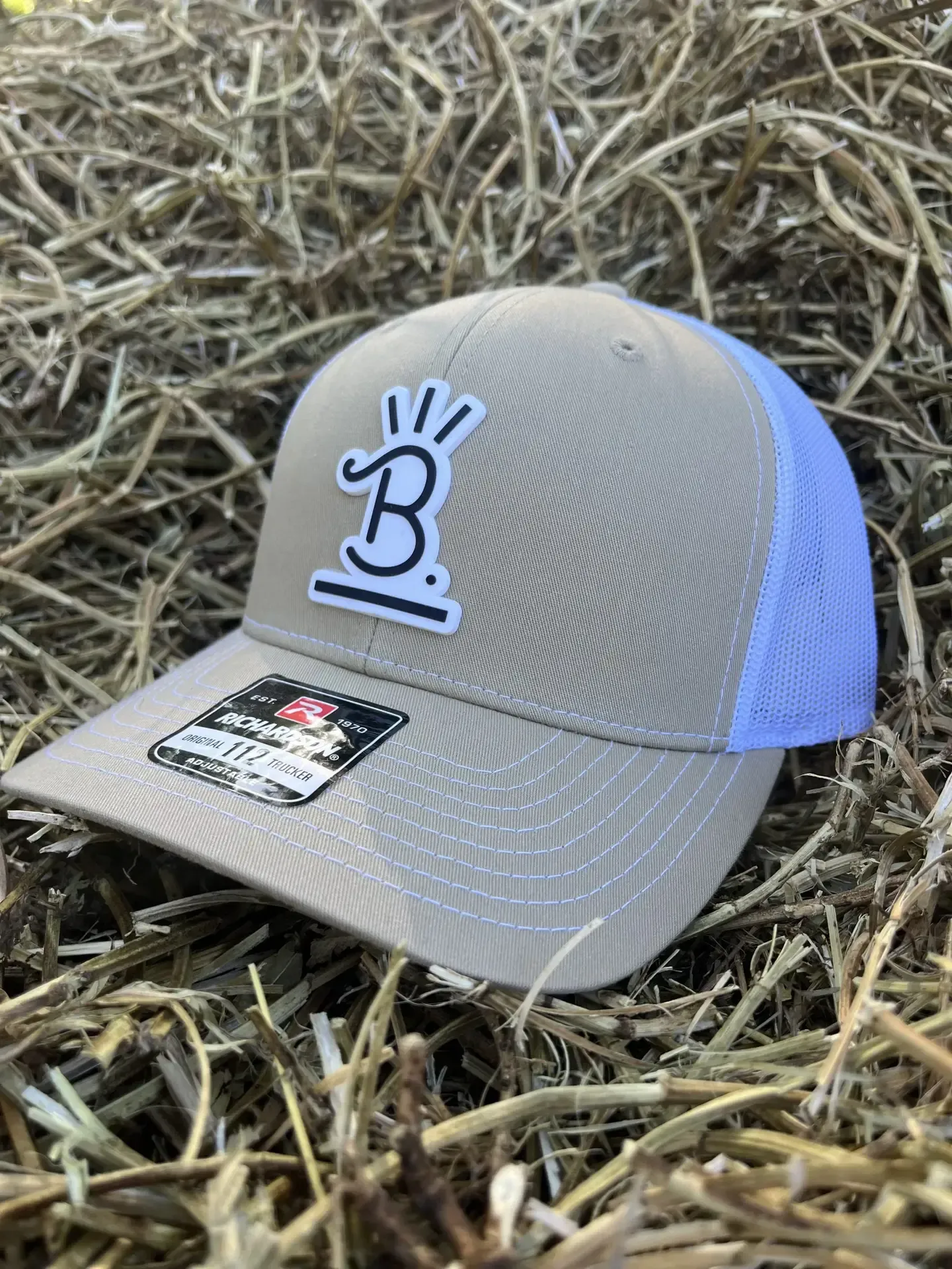 Gray baseball cap with blue mesh back and logo, resting on straw-like ground.