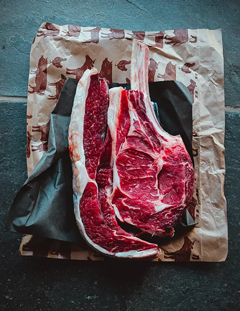 Two raw steaks on butcher paper with a dark cloth on a textured surface