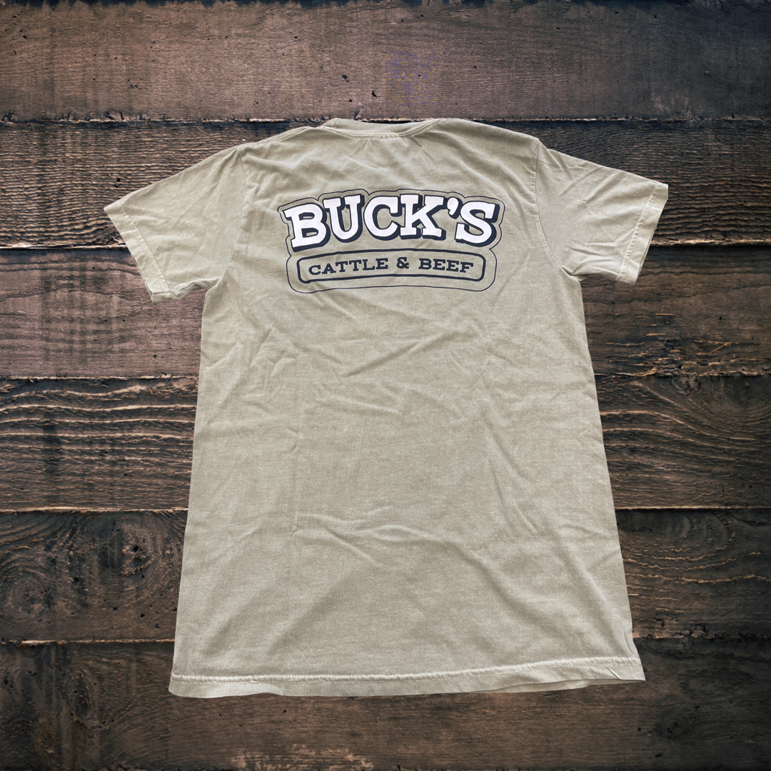 Beige Buck’s Cattle & Beef T-shirt laid flat on a wooden background
