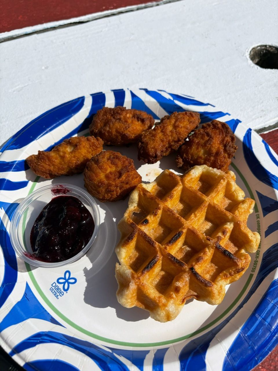 Chicken and waffles meal on paper plate with berry jam.