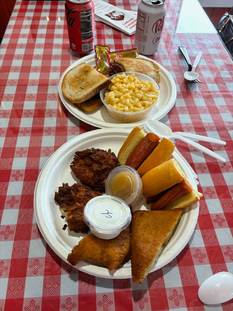Two plates of food, with sandwiches, mac and cheese, and fried items on a red and white checkered tablecloth.