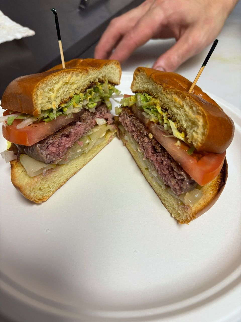 Hamburger cut in half on a white plate, with a person's hand in the background.