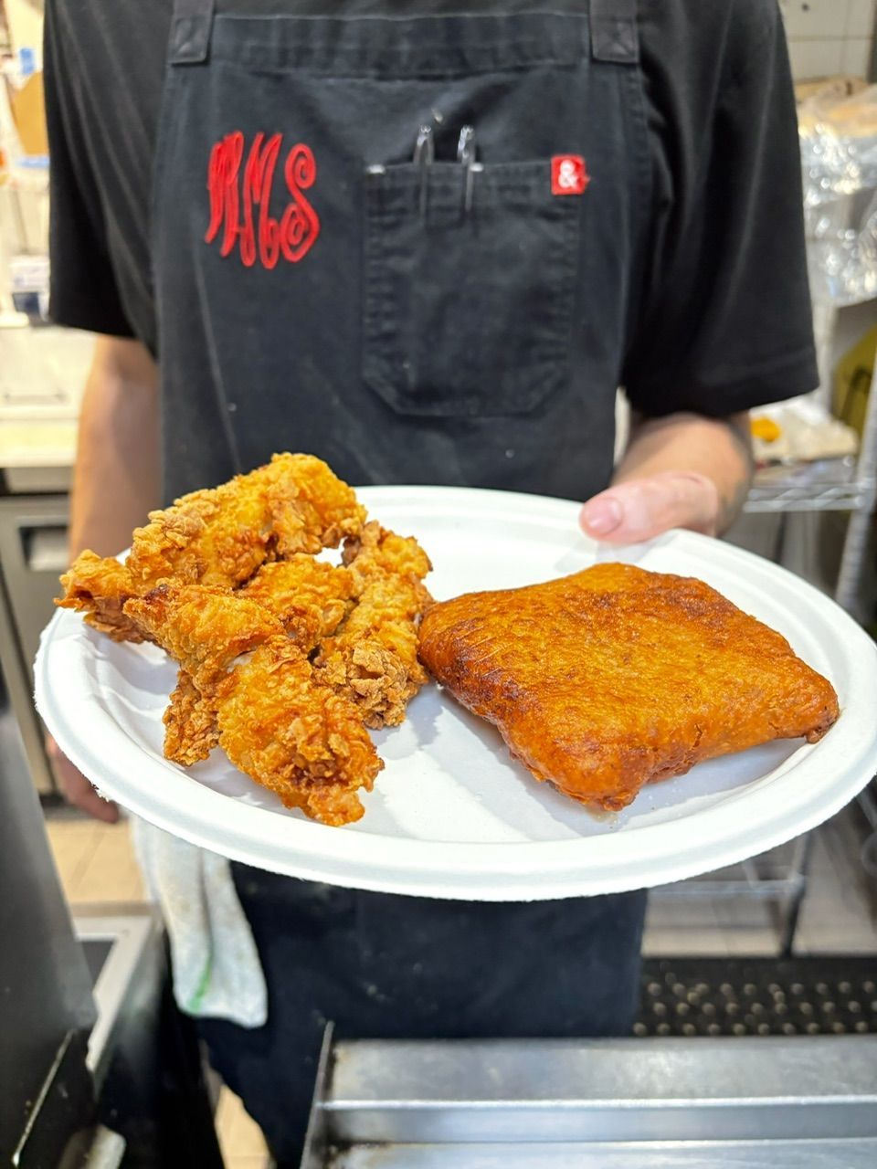 Person holding a paper plate with fried chicken and a fried square.