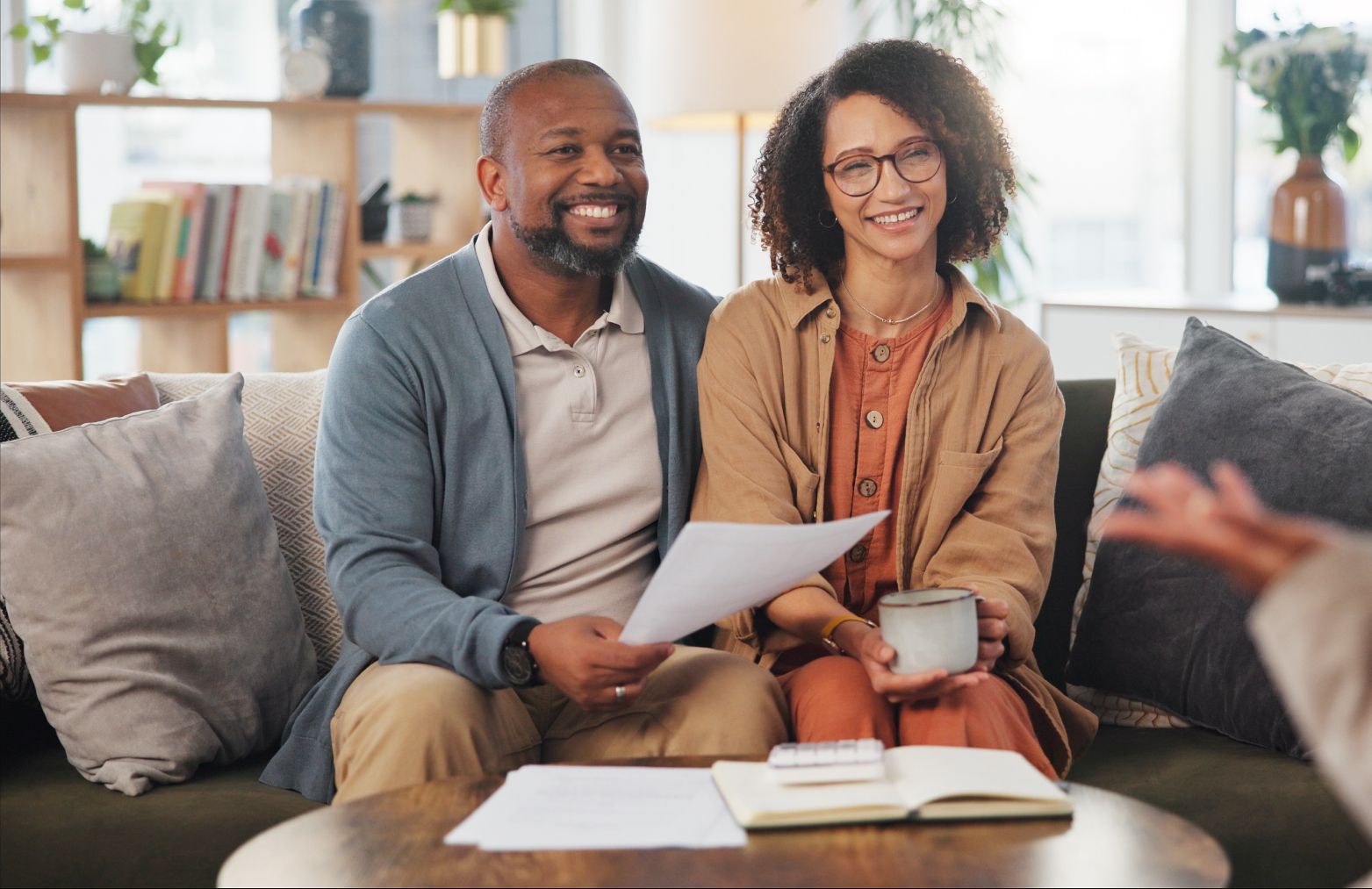 Two people smiling on a couch, reviewing papers in a bright living room with books and a coffee table.