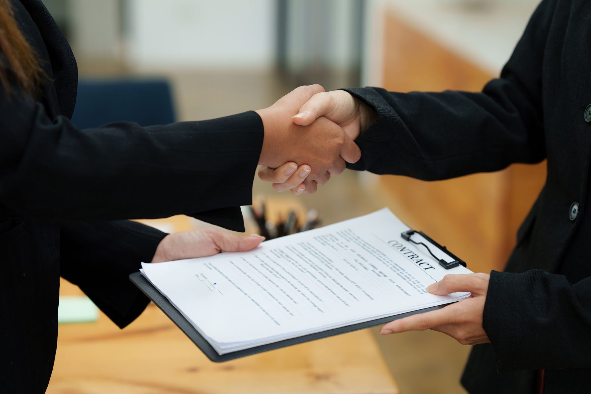 Two people shaking hands over a clipboard with a signed document in a bright office setting