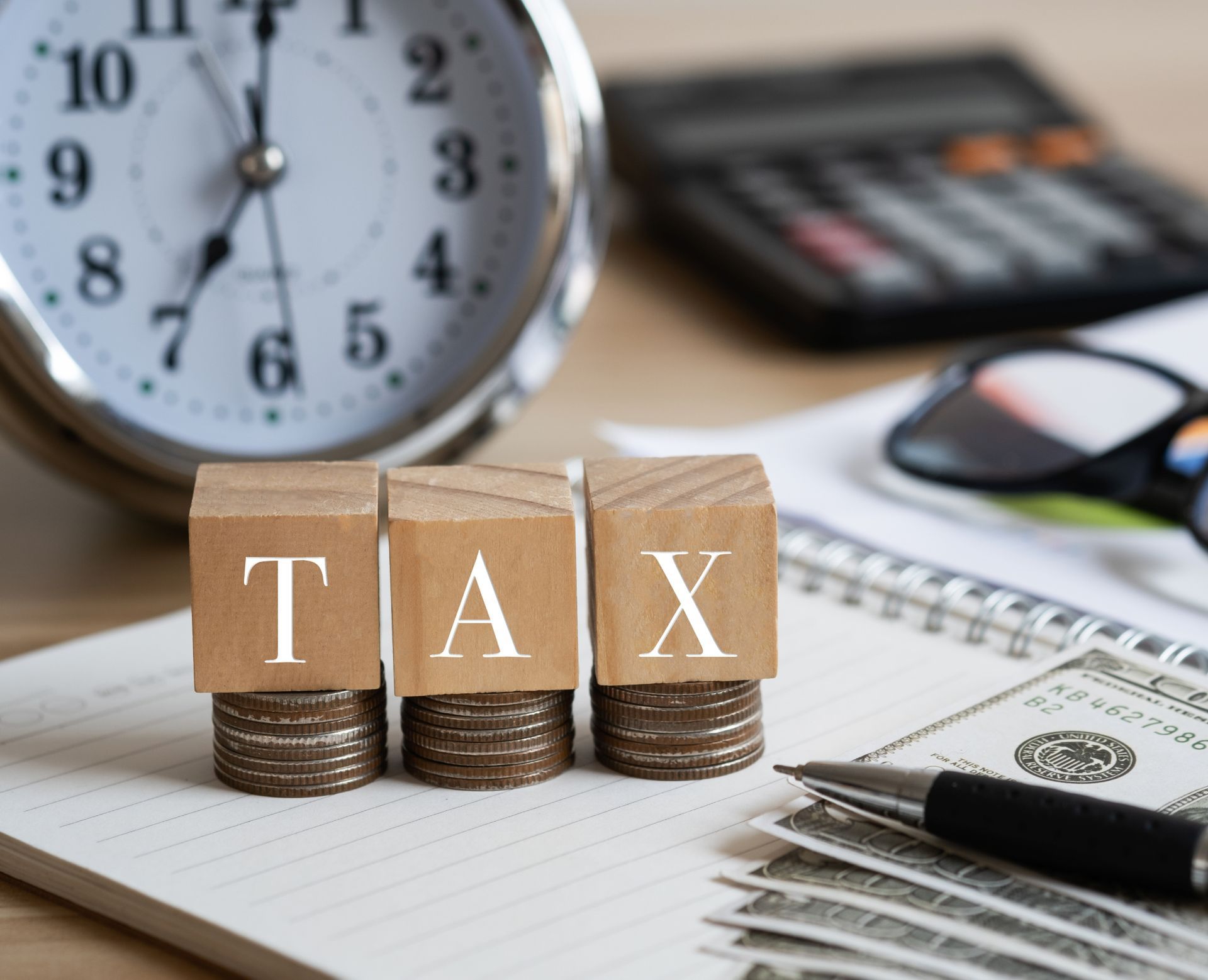 Tax blocks on papers beside a clock, calculator, glasses, and pen on a desk