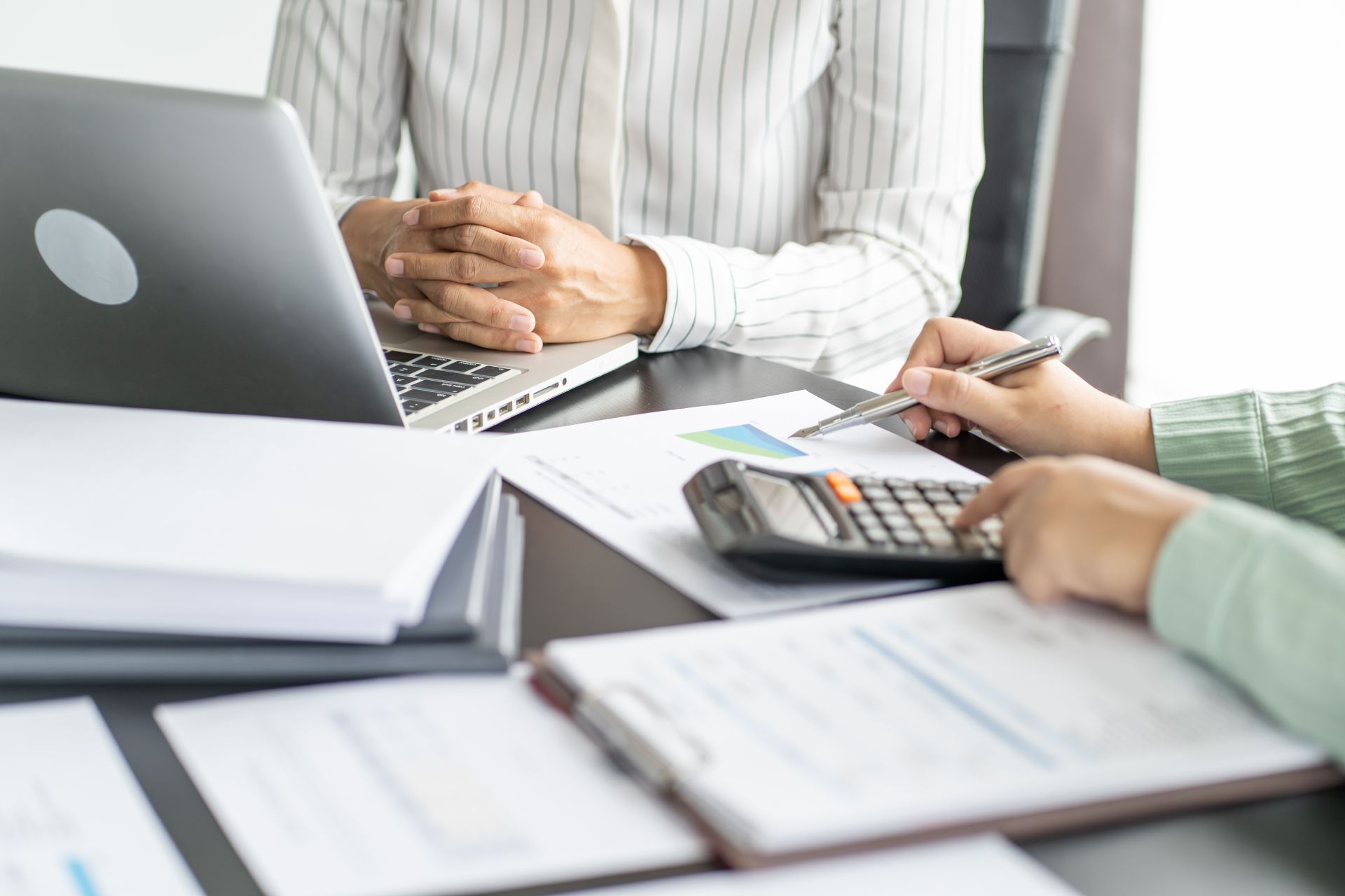 People discussing finances at a desk with a laptop, calculator, and paperwork