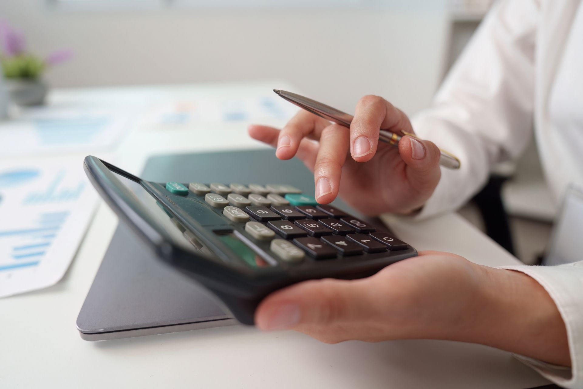 Person using a calculator and holding a pen over financial documents on a desk