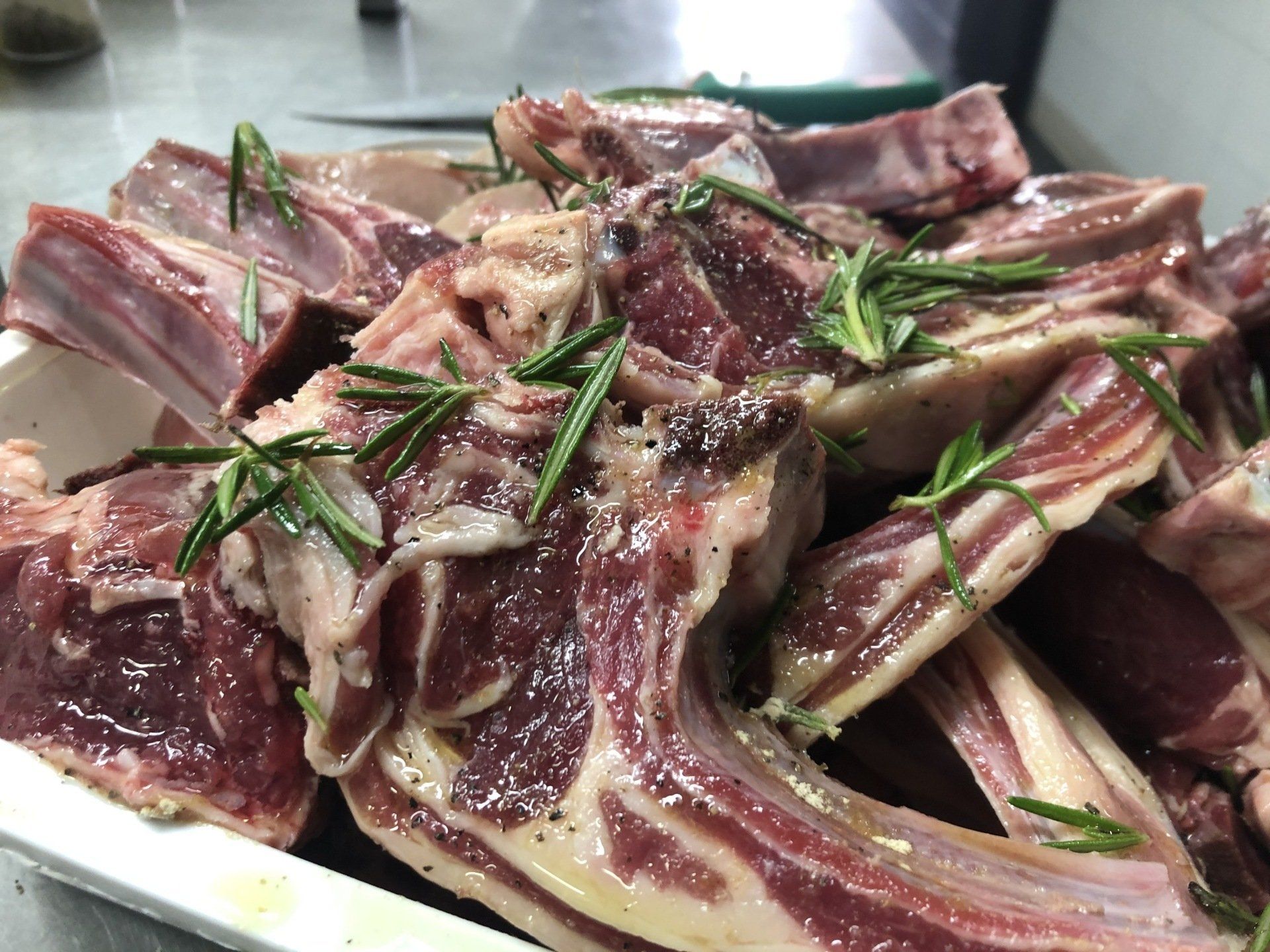 Una pila di costolette di agnello crude con rosmarino su un piatto bianco.