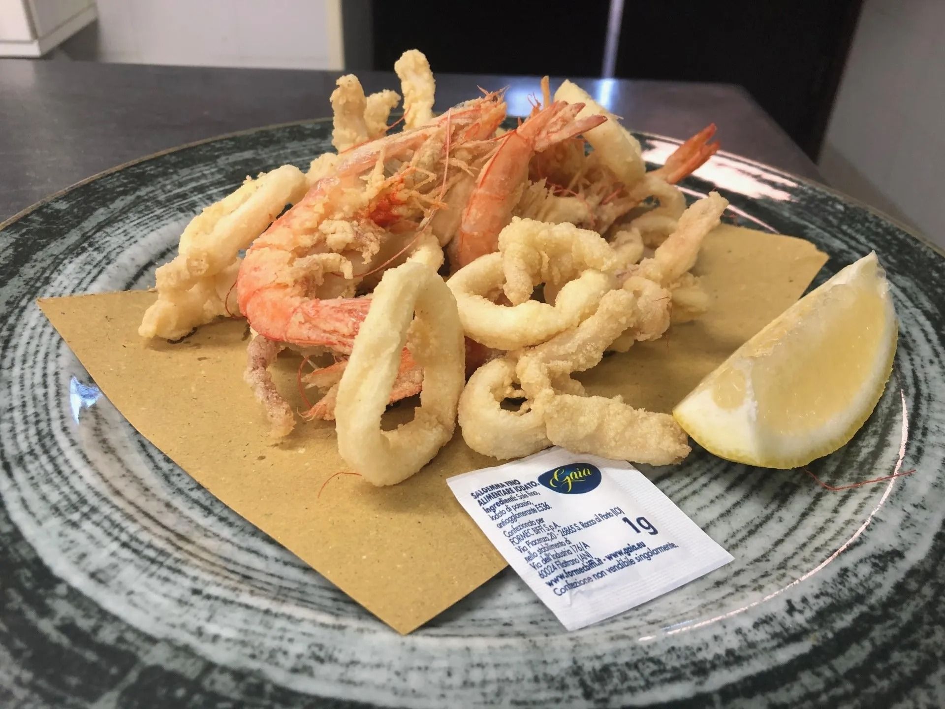 Un piatto di frutti di mare fritti con una fetta di limone su un tavolo.