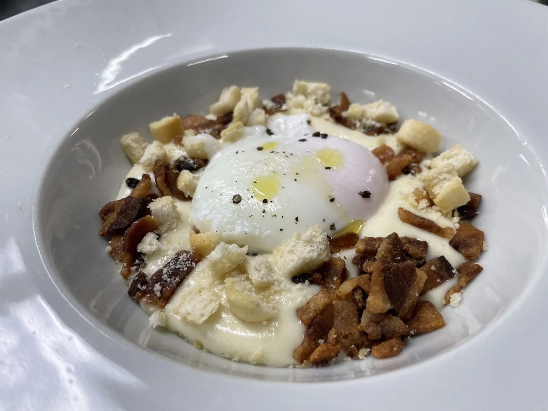 Primo piano di una ciotola di cibo con uova e pancetta su un tavolo.
