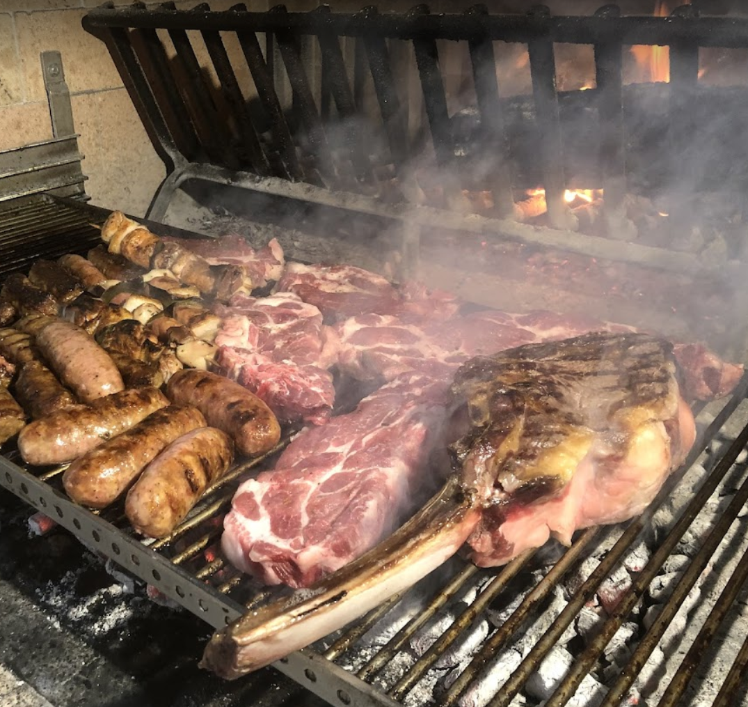 La carne e le salsicce vengono cotte su una griglia da cui esce del fumo