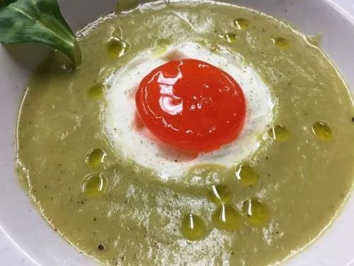 Primo piano di una ciotola di zuppa con un pomodoro sopra.