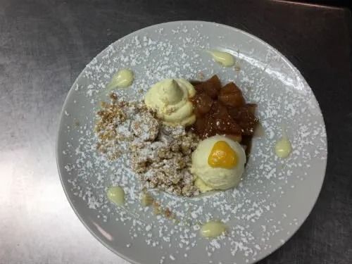 Un piatto bianco sormontato da un dessert e da un gelato su un tavolo.