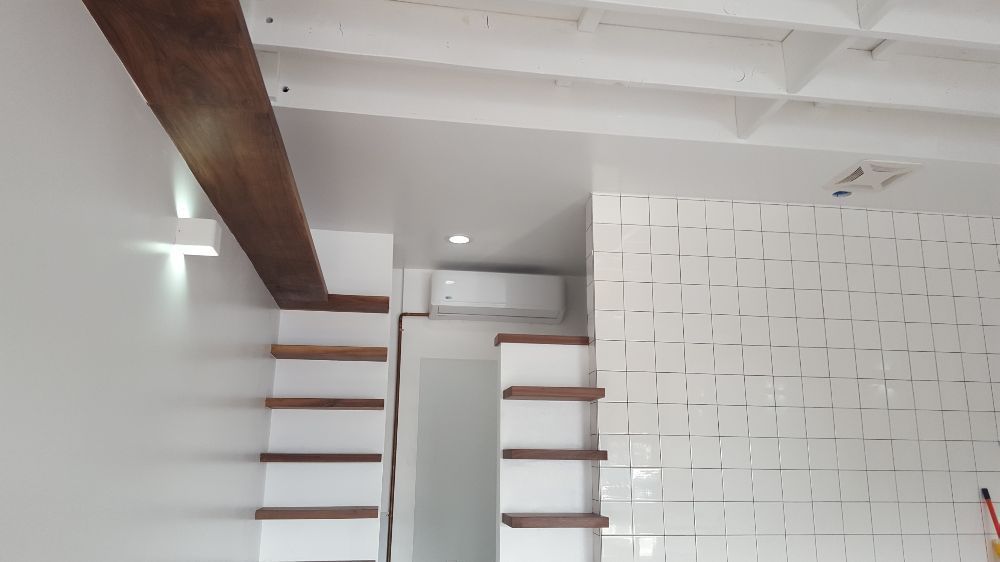 Outdoor air conditioner unit beside a gray house wall and wooden fence.