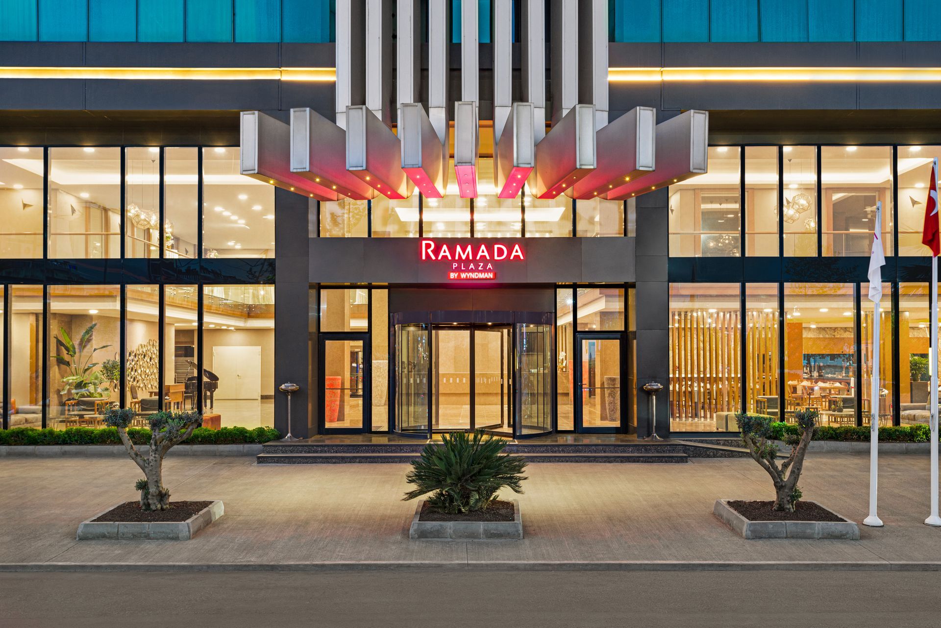 Ramada Plaza Samsun | Ramada otelinin girişi, alacakaranlıkta, parlak kırmızı tabelası, cam kapıları.