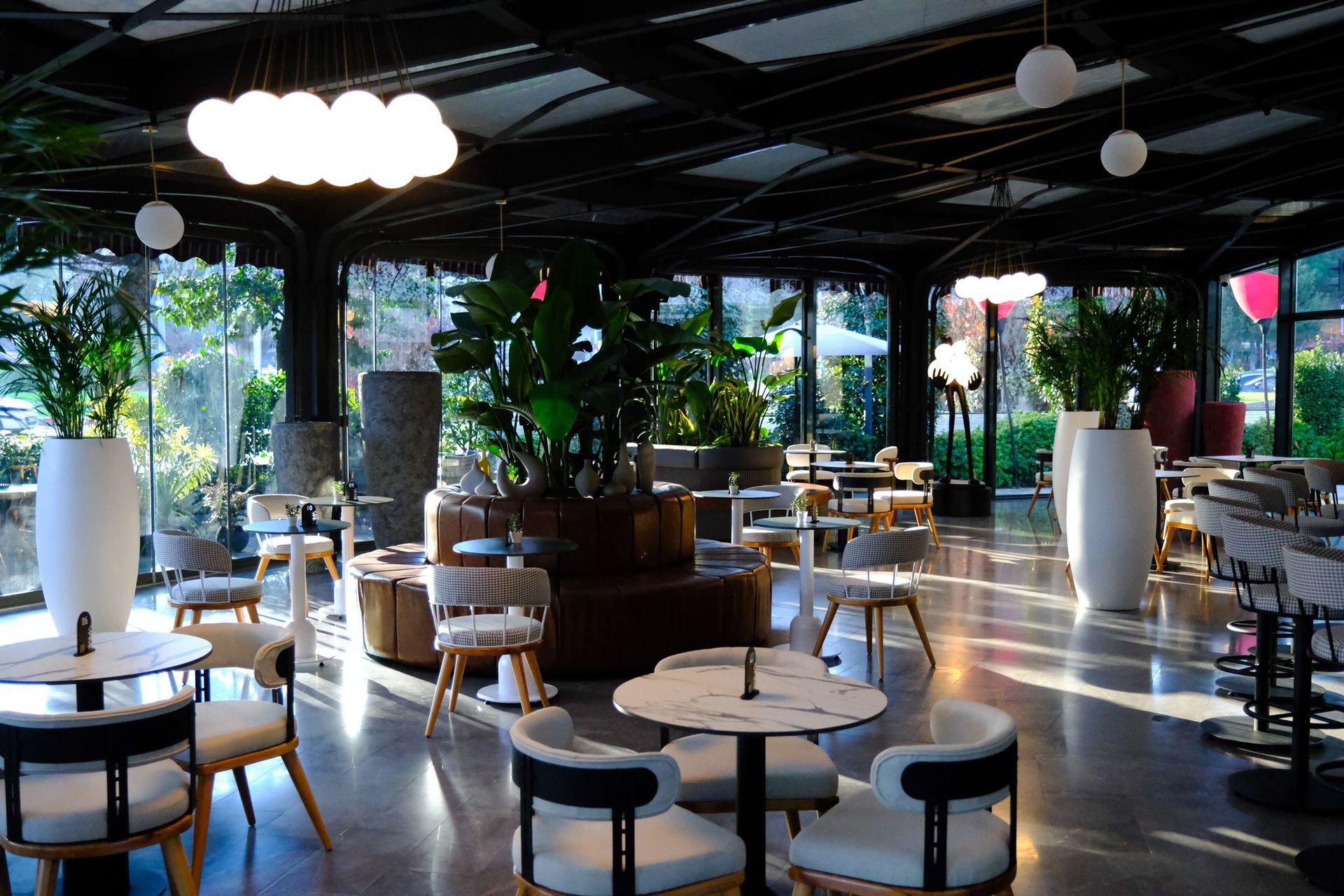 Ramada Plaza Samsun | Masalar, tabureler, bitkiler ve büyük pencerelerle donatılmış modern restoran iç mekanı.