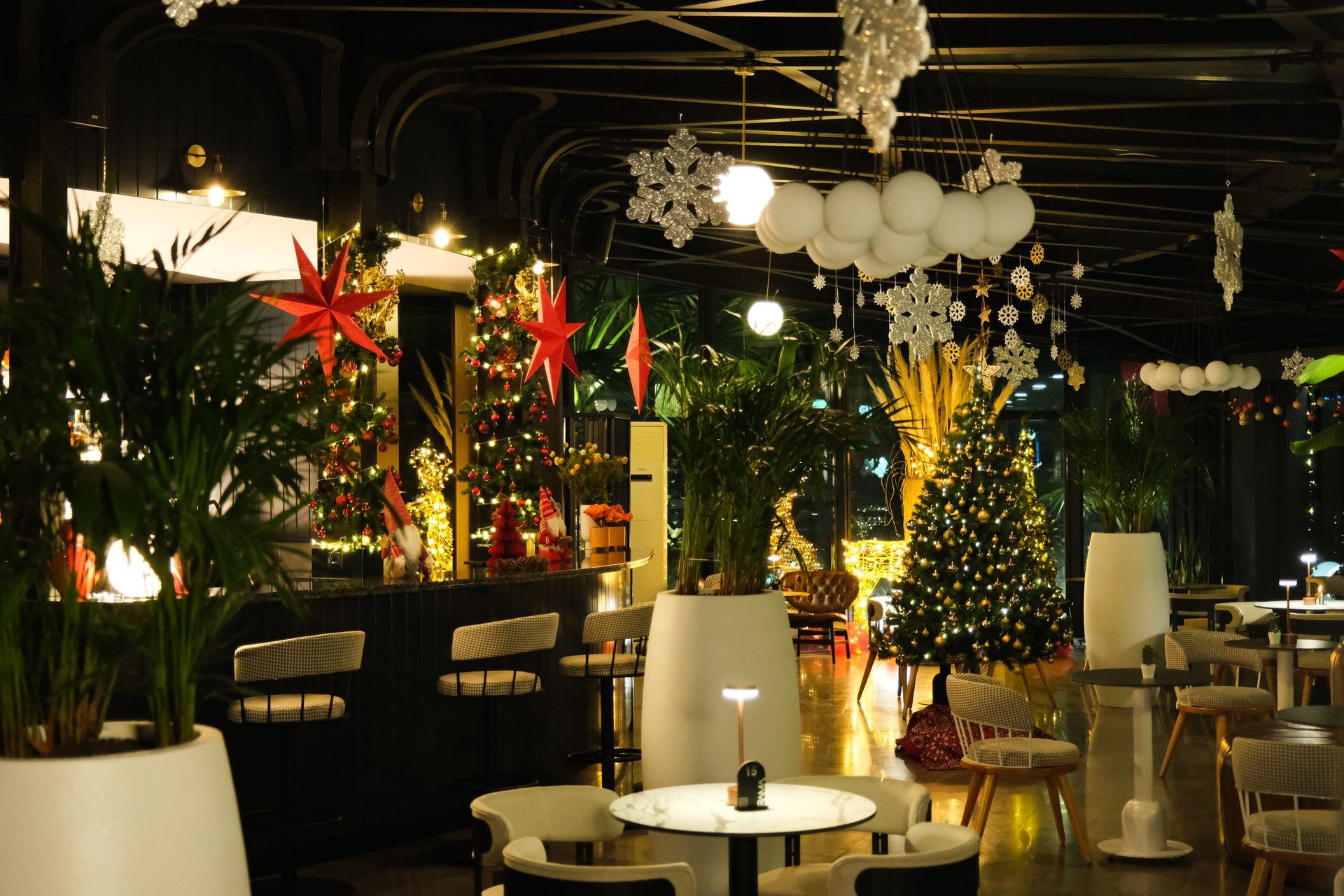 Noel ağaçları, asılı ışıklar ve kırmızı yıldız süslemeleriyle şenlikli bir restoran salonu.
