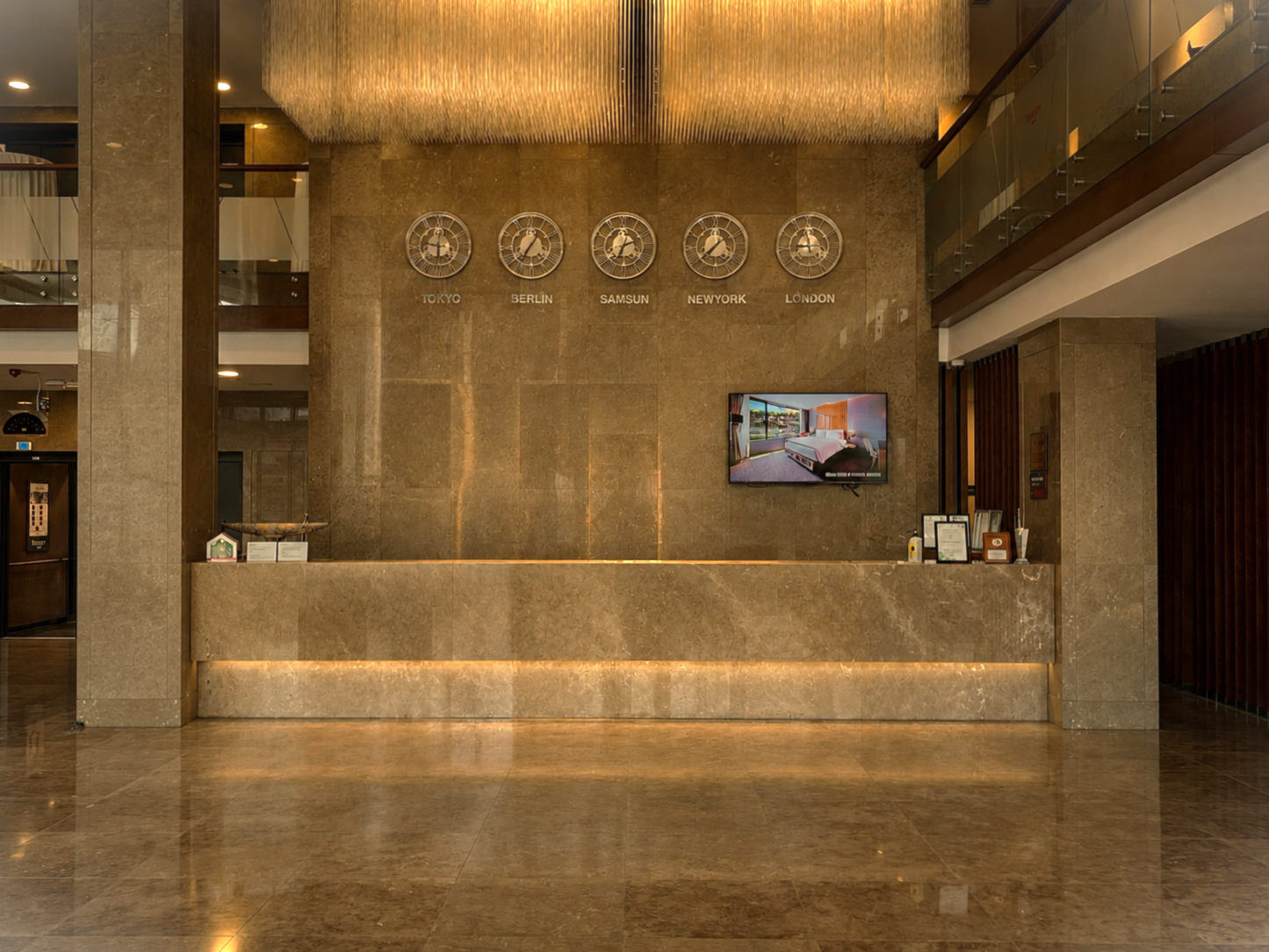 Ramada Plaza Samsun |  Mermer resepsiyon masası, sıcak aydınlatma ve  televizyon bulunan, modern otel lobisi.
