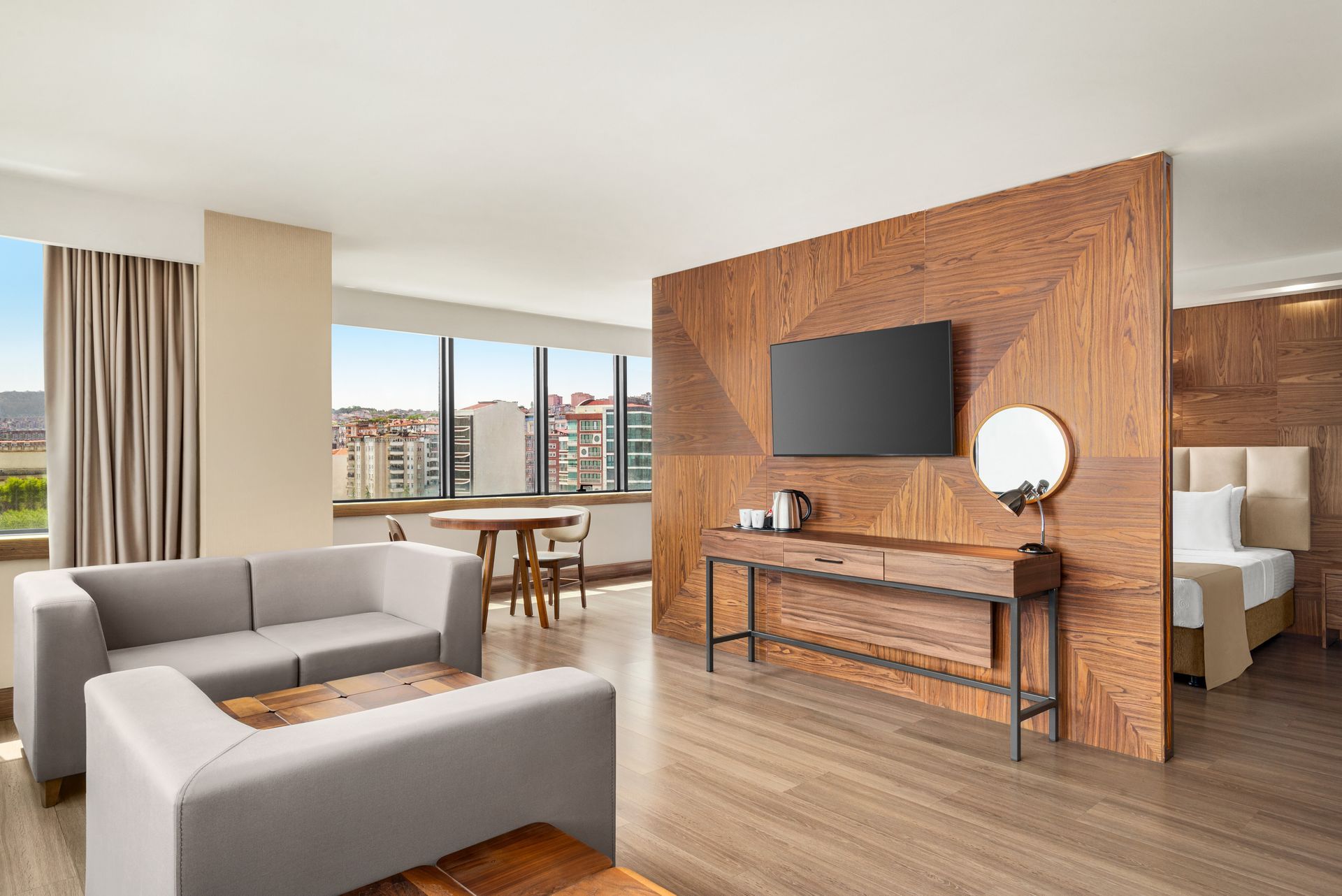 Ramada Plaza Samsun | Gri kanepeler, ahşap vurgu duvarı ve büyük pencerelerden şehir manzarası sunan modern oturma odası.