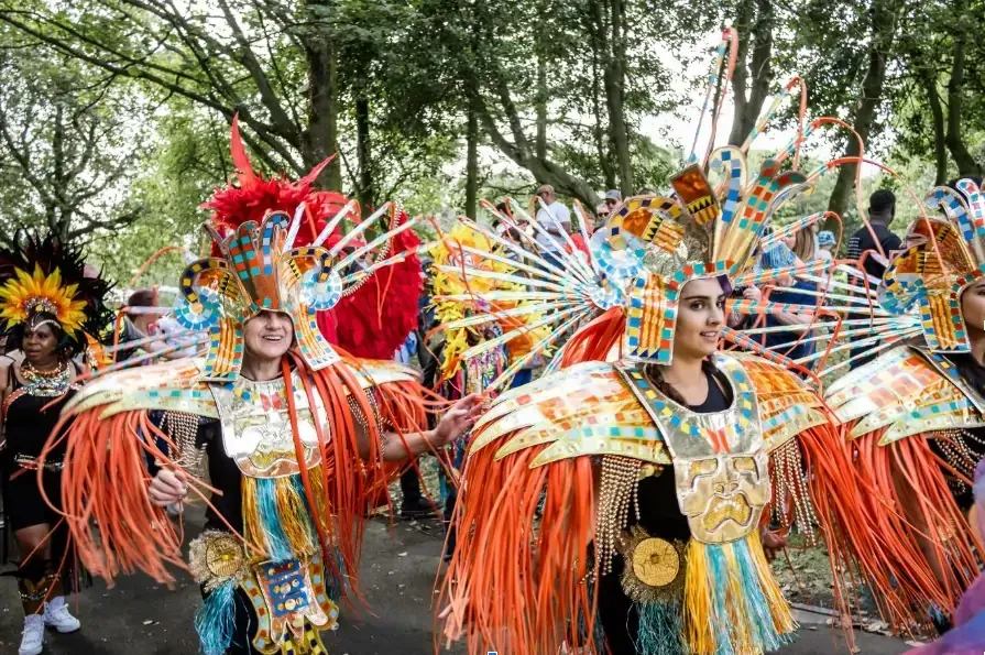 People in vibrant costumes dance in a parade, featuring gold, orange, and blue accents.