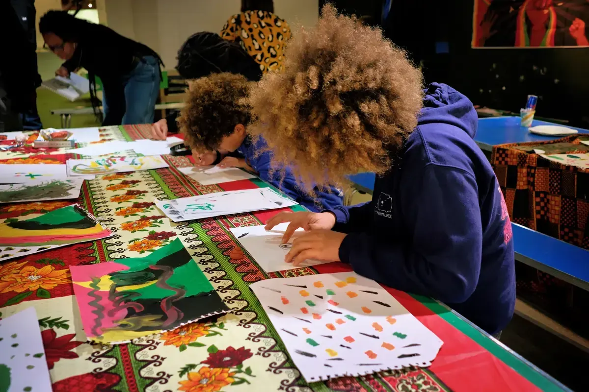 People with afro hair draw and paint at a table covered with colorful fabric.
