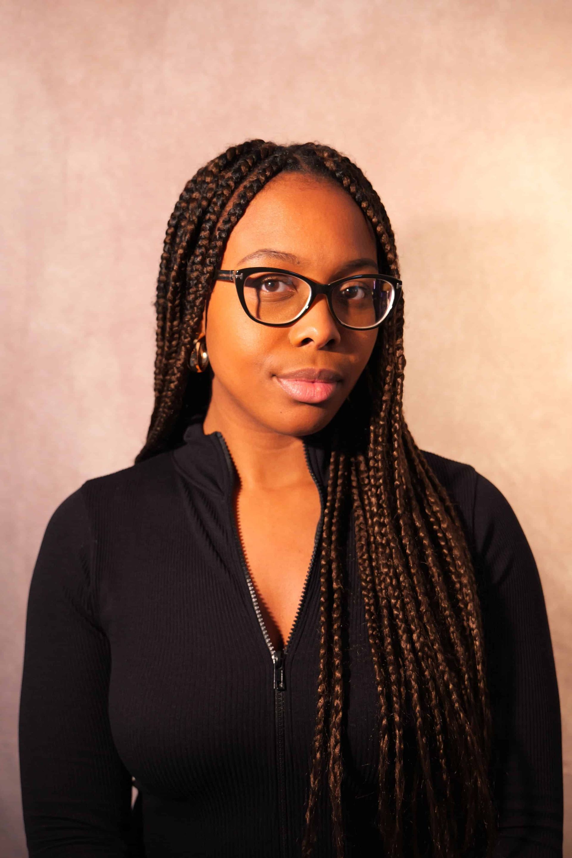 Young Black woman with glasses and long braids wearing a black top, looking at the camera.