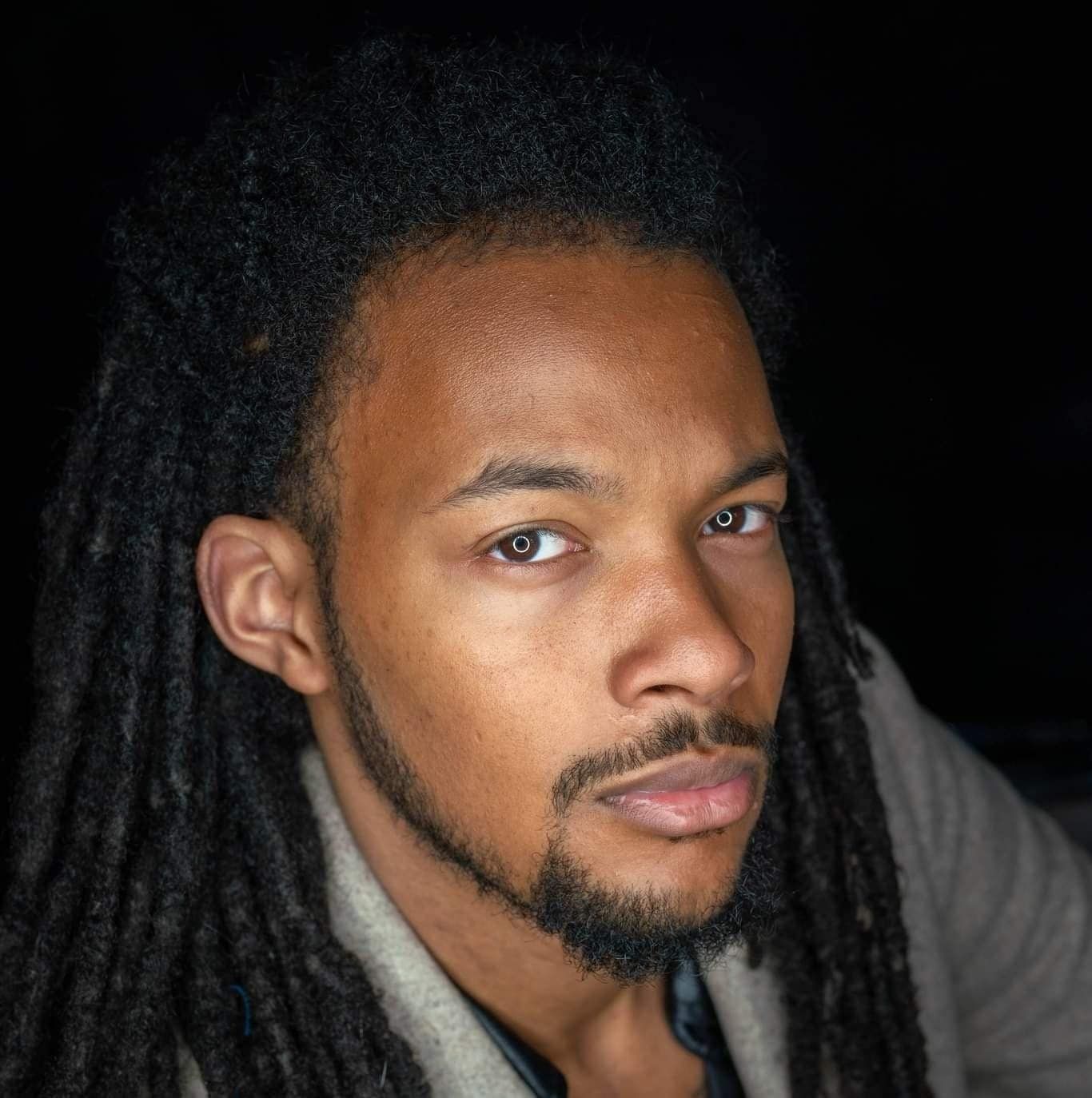 Man with long dreadlocks and beard, looking at camera with a neutral expression.