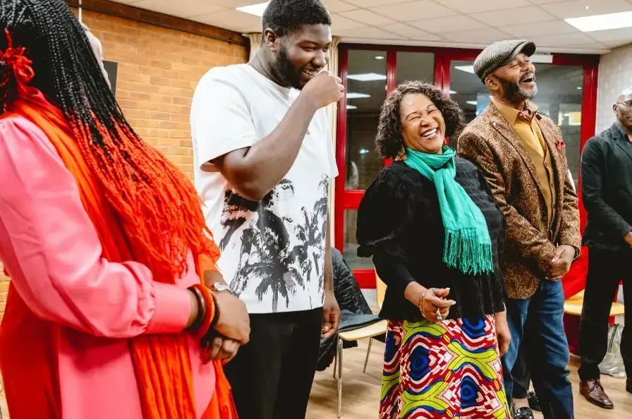 Group of people laughing together in a room; diverse faces and colorful clothing.
