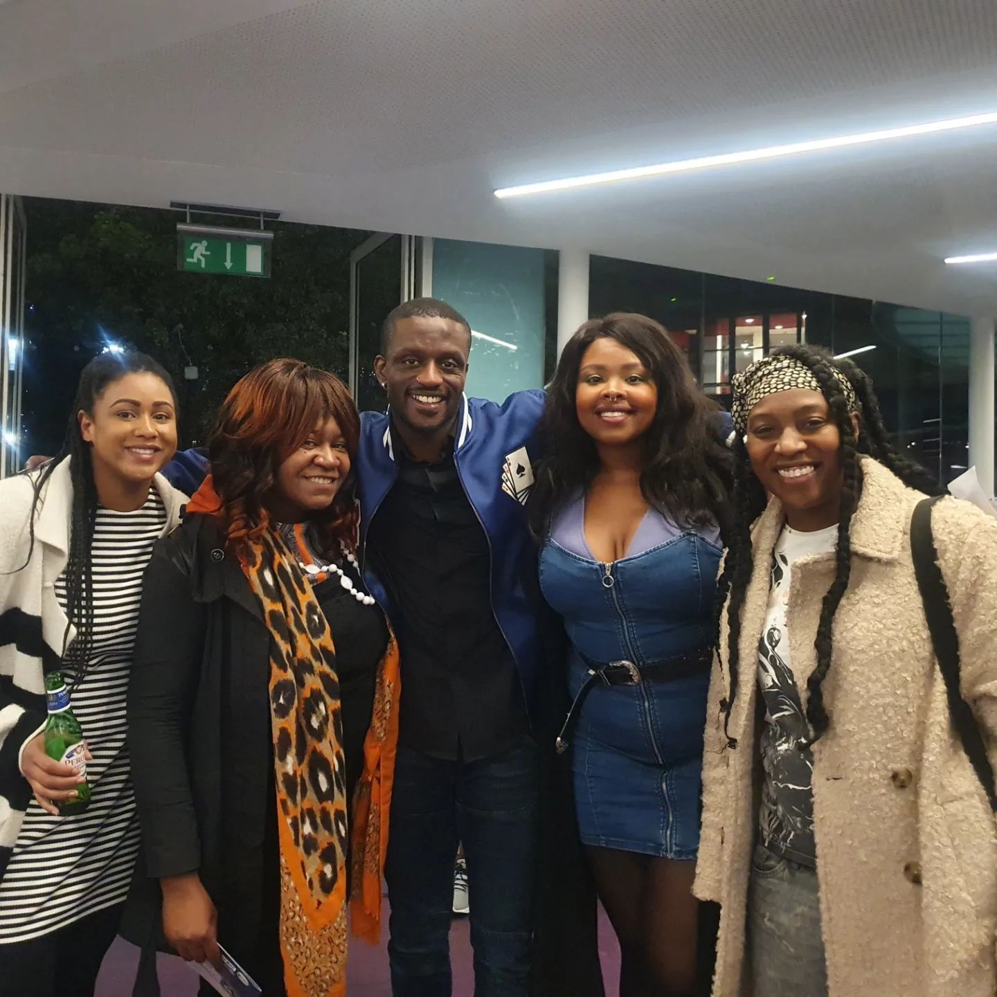 Five people smiling at the camera. A man in a blue jacket stands amongst the women. Indoors.