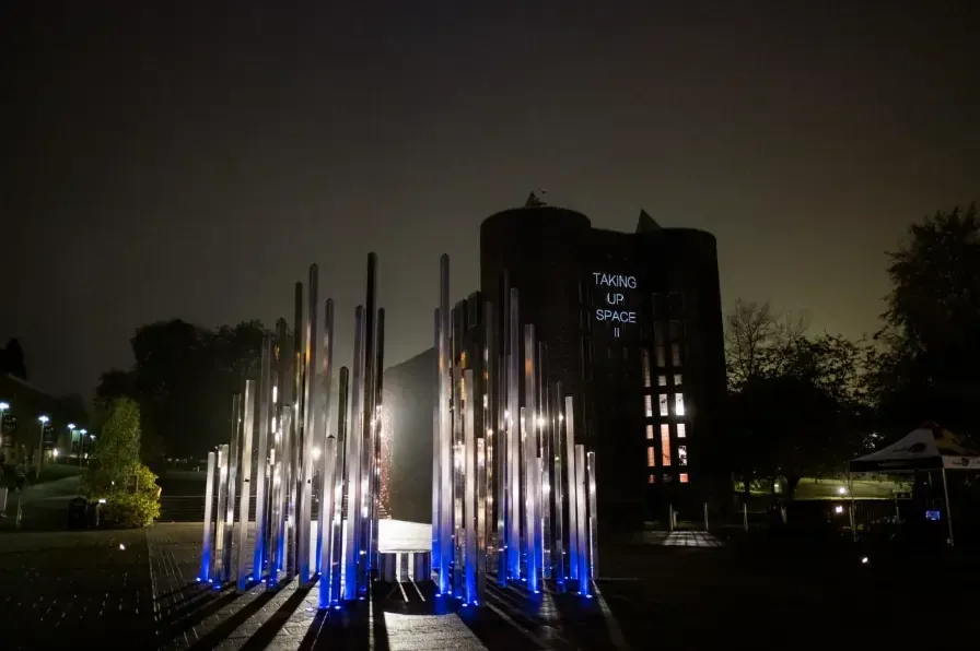 Night scene with illuminated metal sculptures, tower, and text 