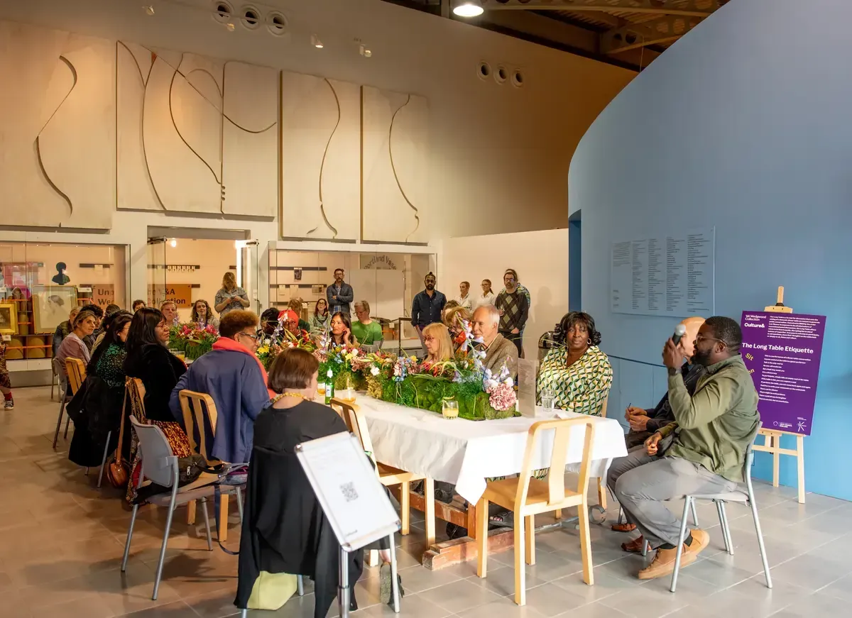 People gathered around a table, attending an event in an art gallery.