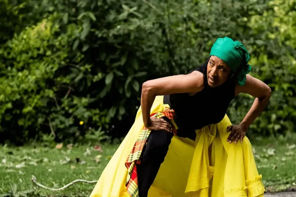 Woman in green headscarf and yellow skirt dances outdoors.