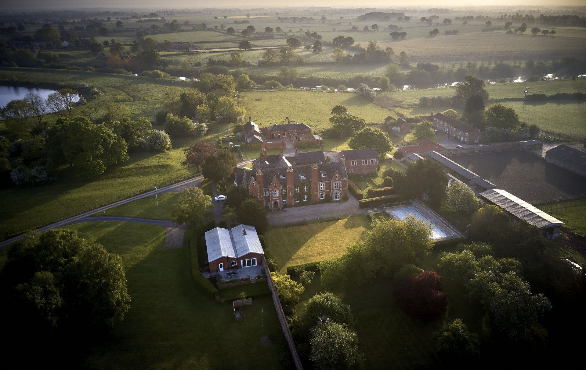An aerial view of a large house in the middle of a lush green field.