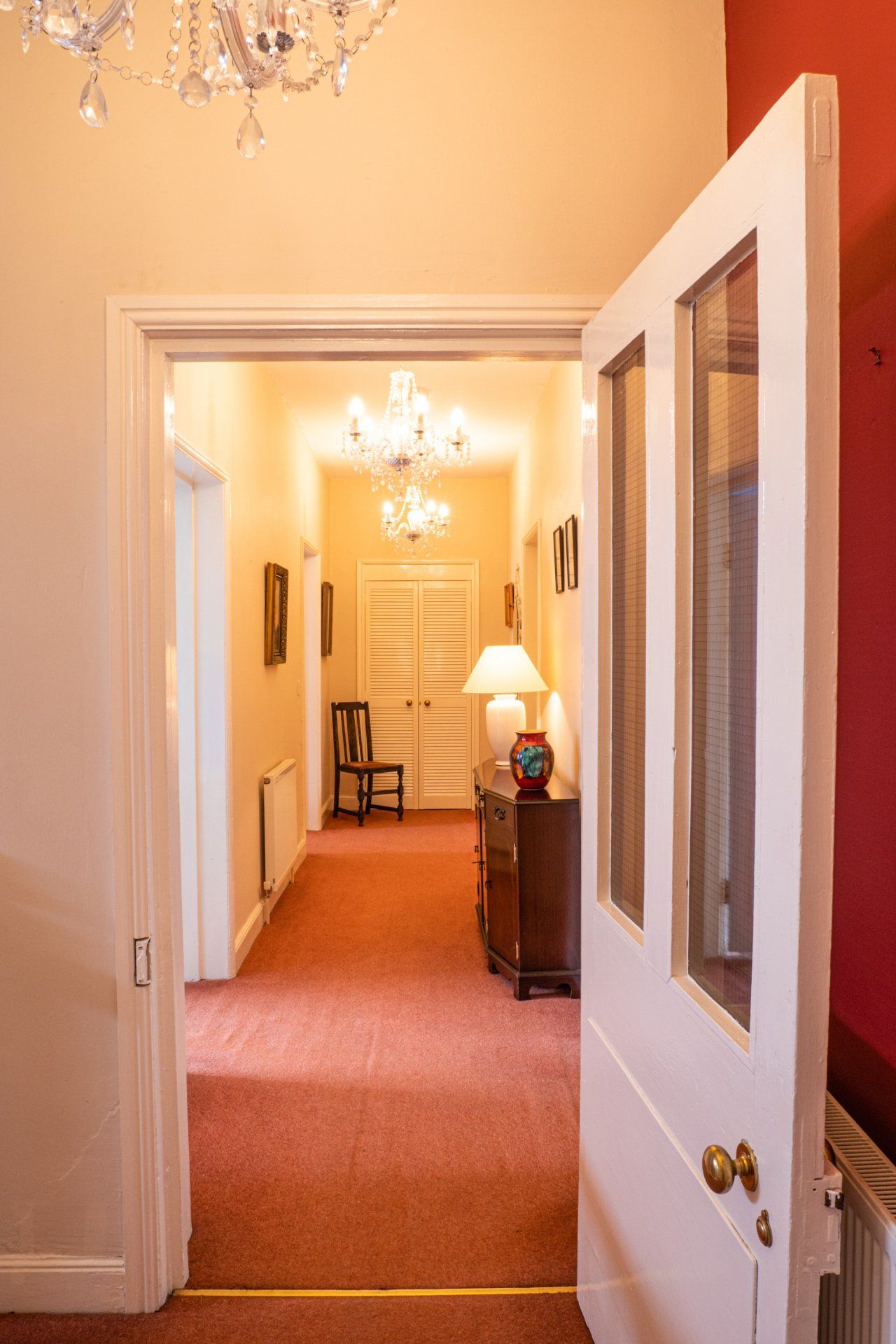 A hallway with a white door open and a red carpet.