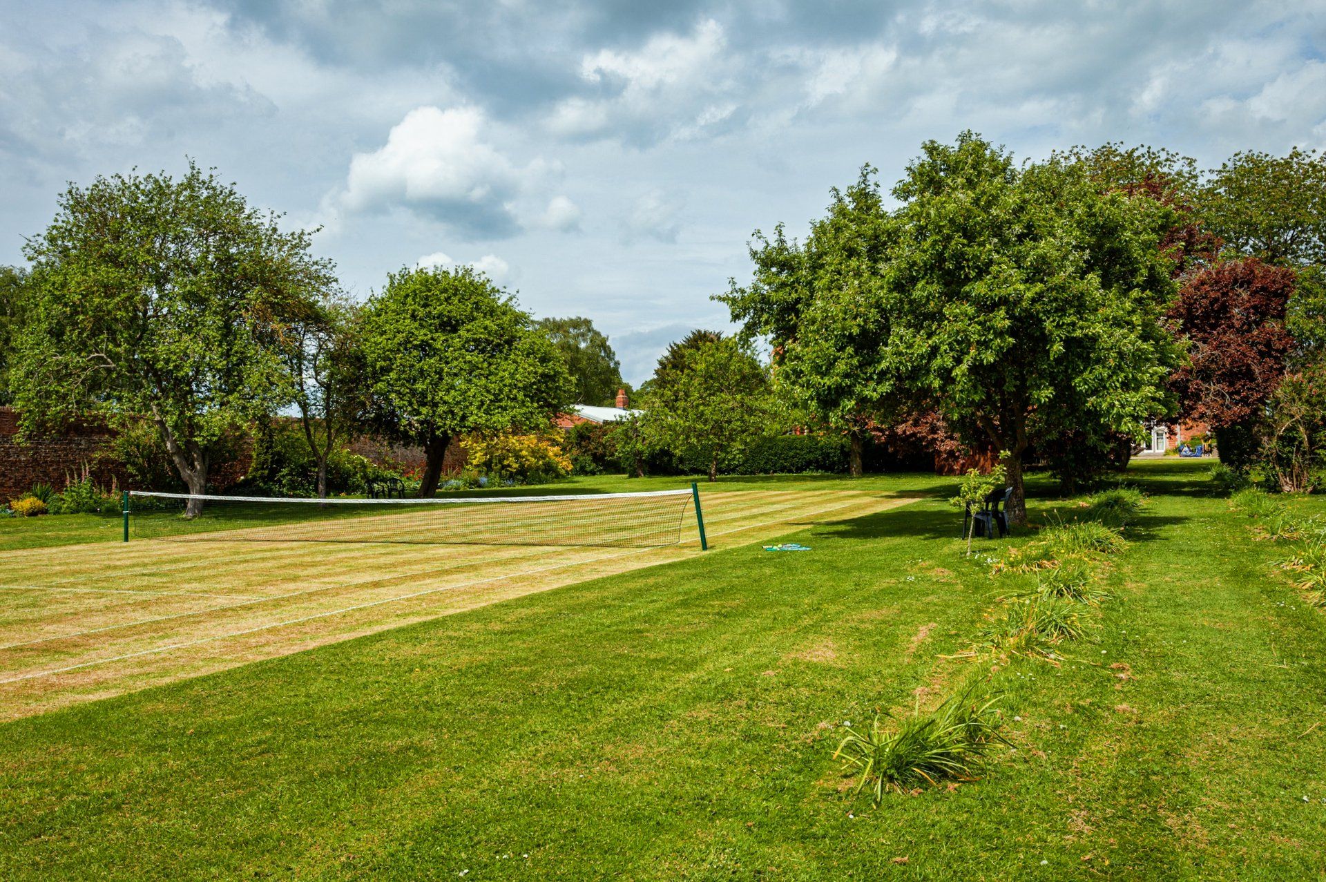 A lush green field with trees and a tennis court in the background