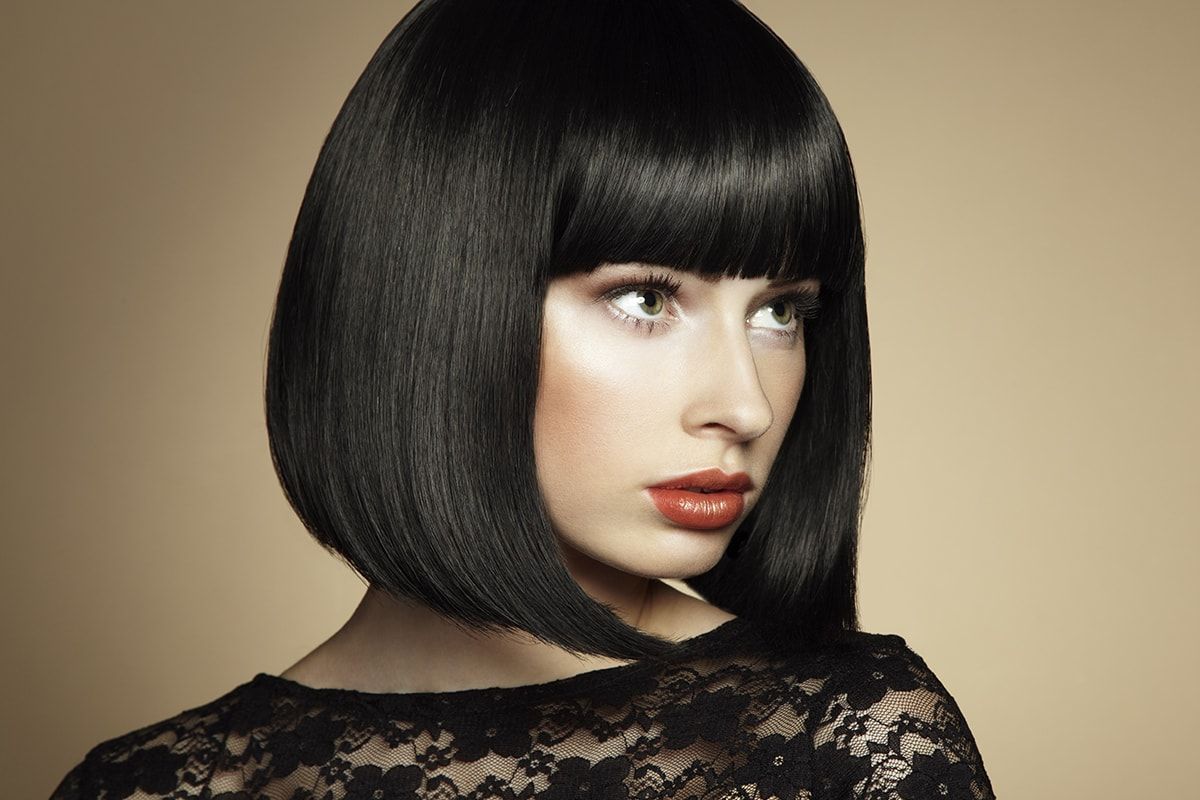 A woman with a bob hairstyle and bangs is wearing a black lace dress.