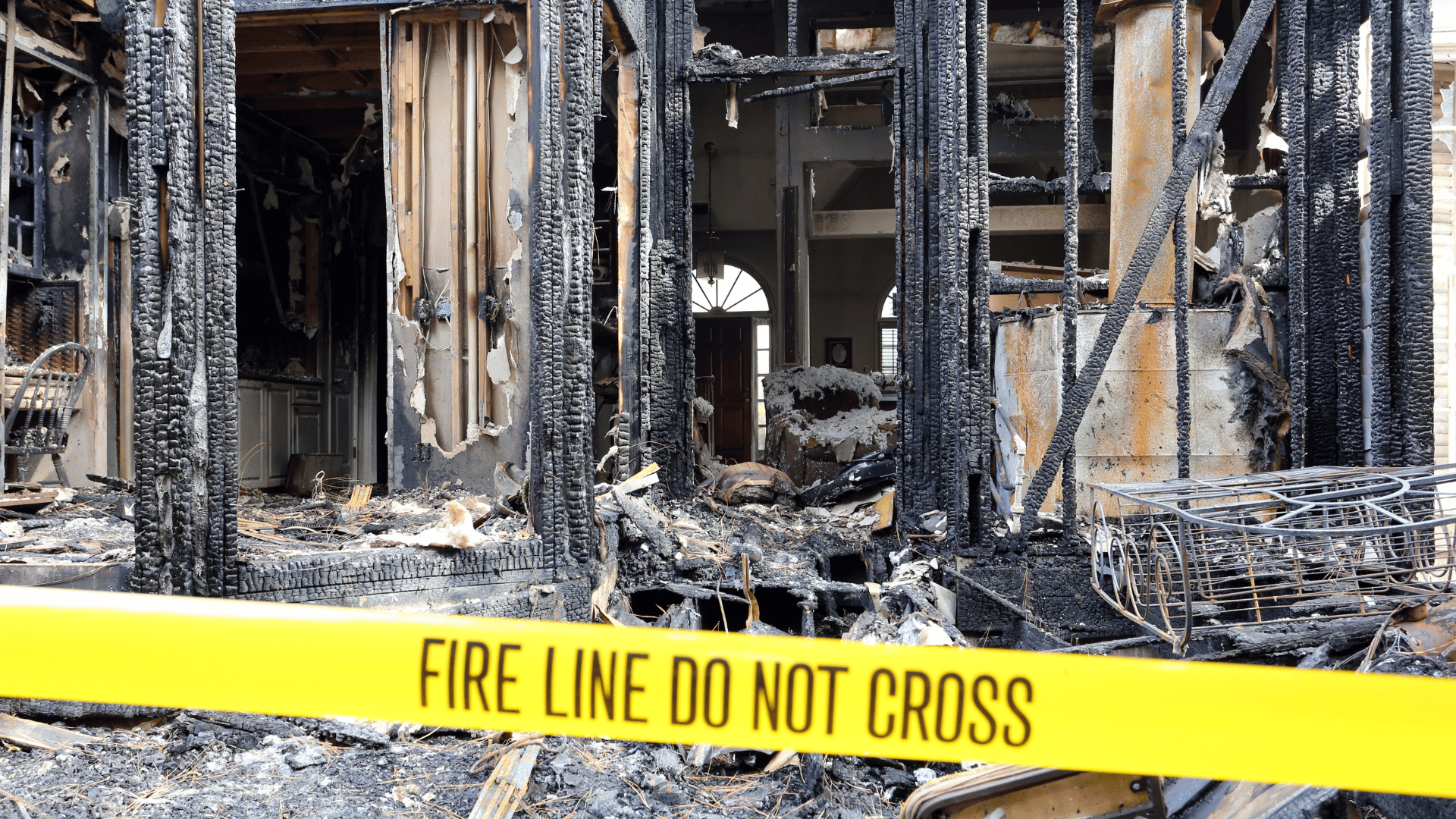 Burned building interior behind yellow fire line tape reading “FIRE LINE DO NOT CROSS”
