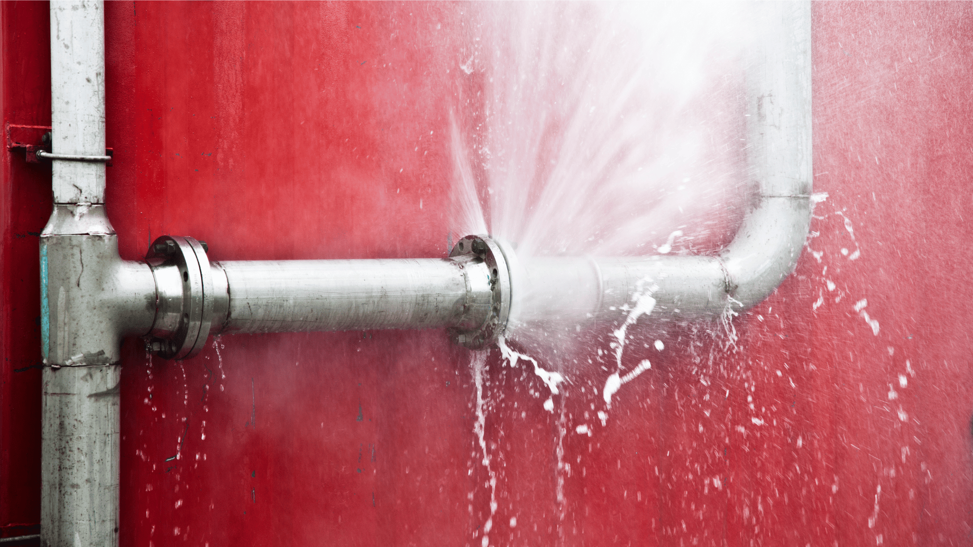 Burst pipe spraying water against a red wall. HRS Restoration Services Denver