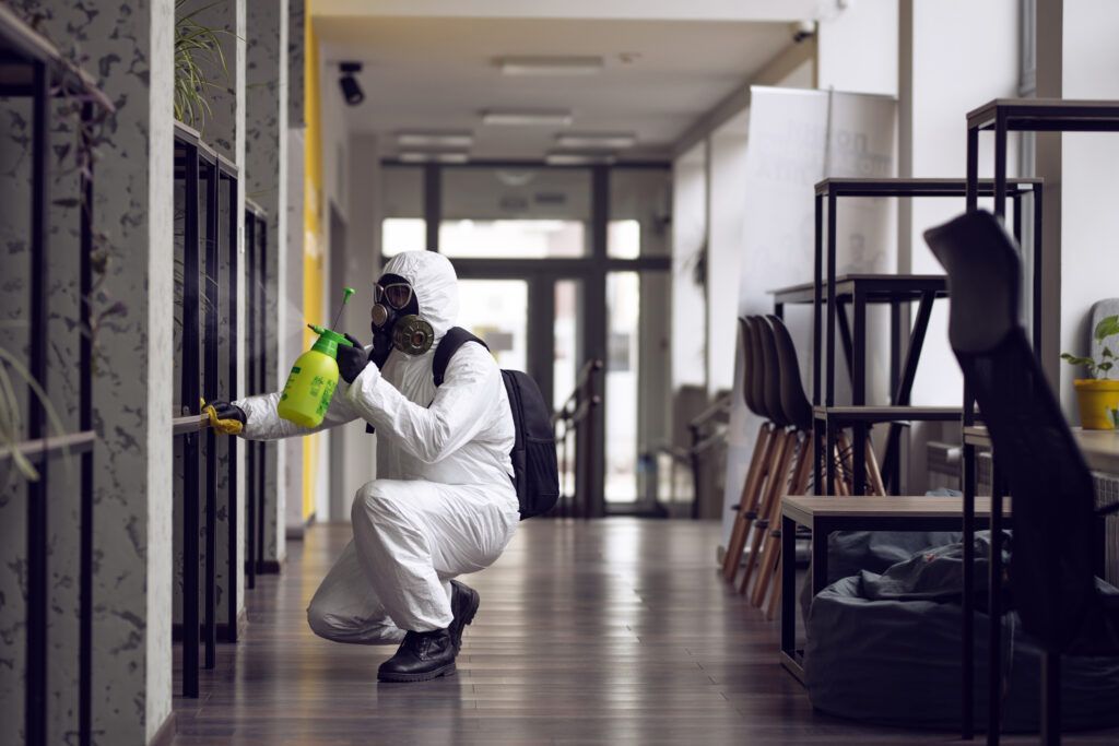 Person in hazmat suit spraying disinfectant in a hallway.