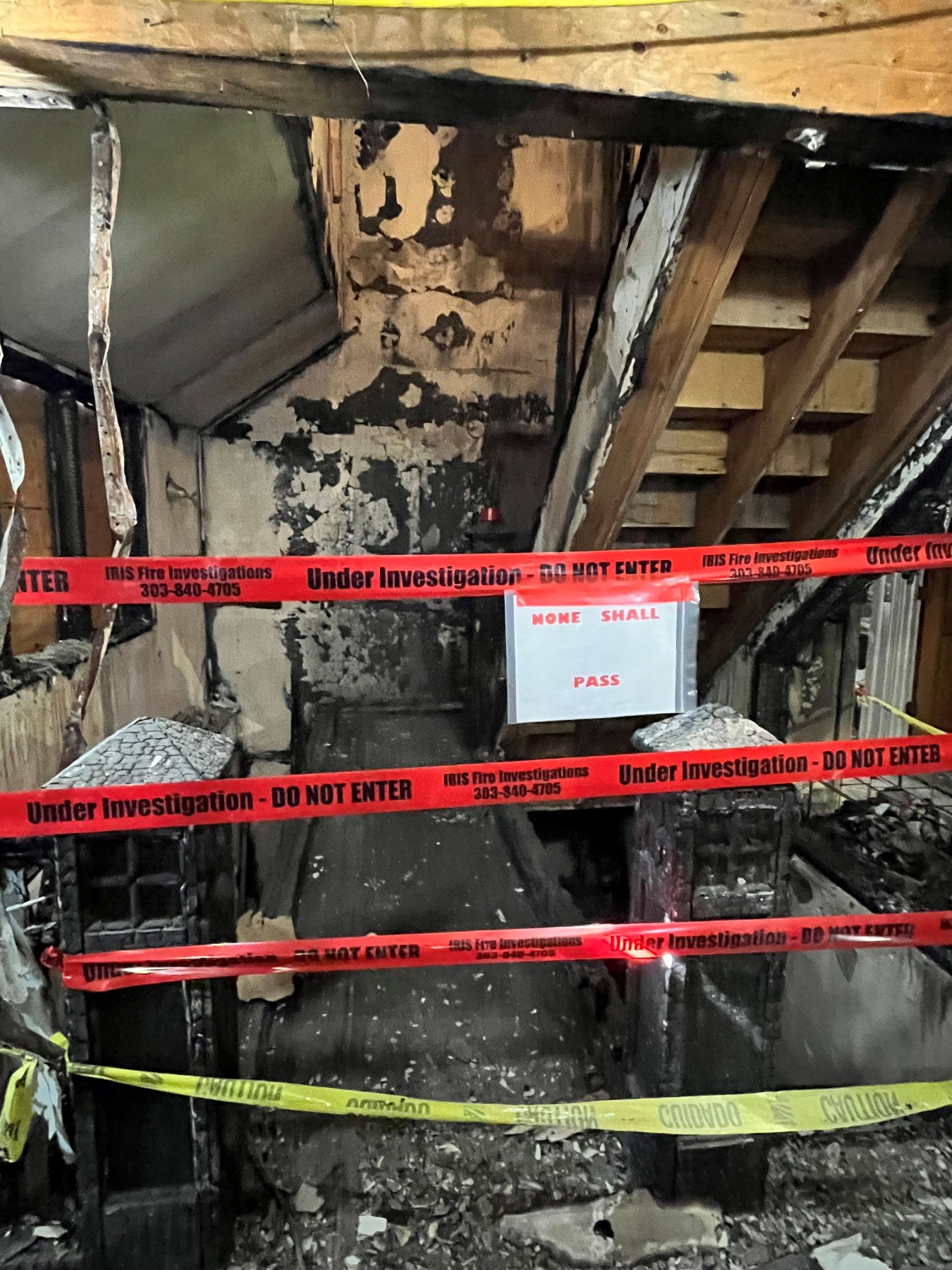 Fire-damaged interior with caution tape. Charred walls, exposed beams, and a staircase - HRS Restoration in Littleton, CO.
