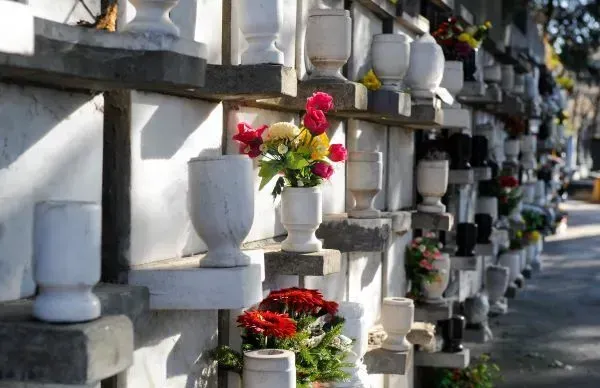 Row of white cemetery niches with colorful flower bouquets along a walkway
