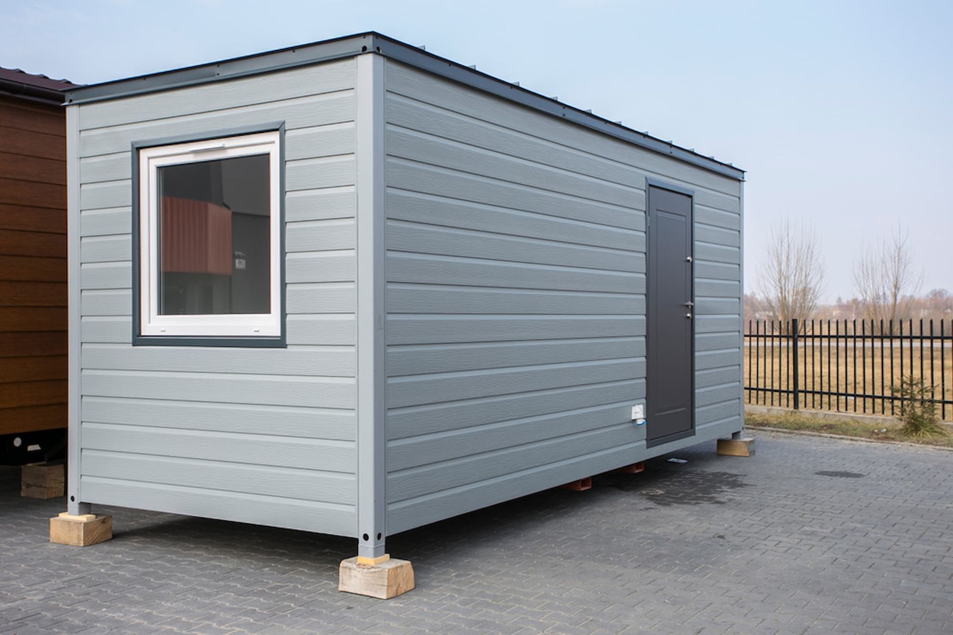 A Small Gray Building with A Window and Door Is Parked in A Parking Lot — ShedPro Constructions in Darawank, NSW