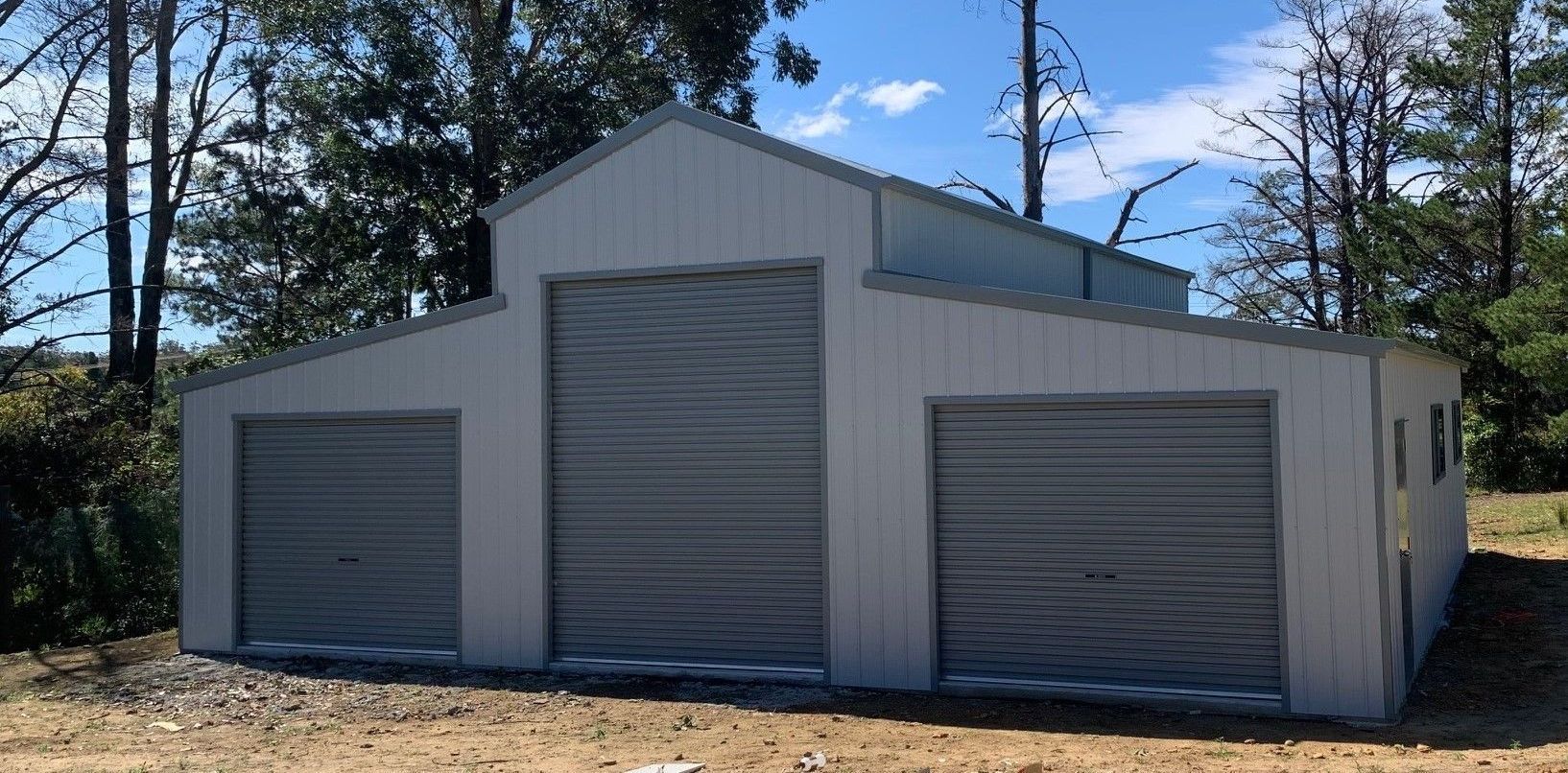 A Barn With Two Garage Doors is Sitting in the Middle of a Dirt Field — ShedPro Constructions in Mid North Coast, NSW